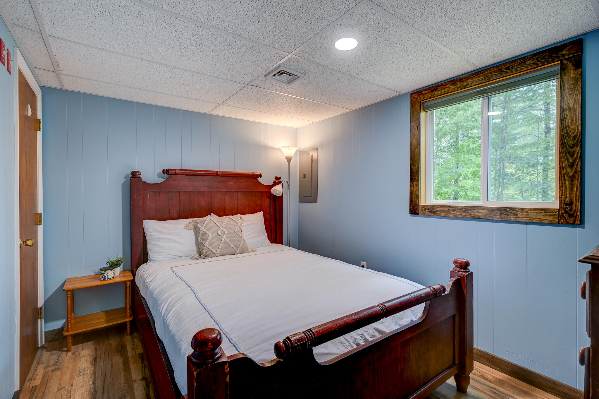 Bedroom with a dark wood four-poster bed, blue walls, and a large wood-trimmed window.