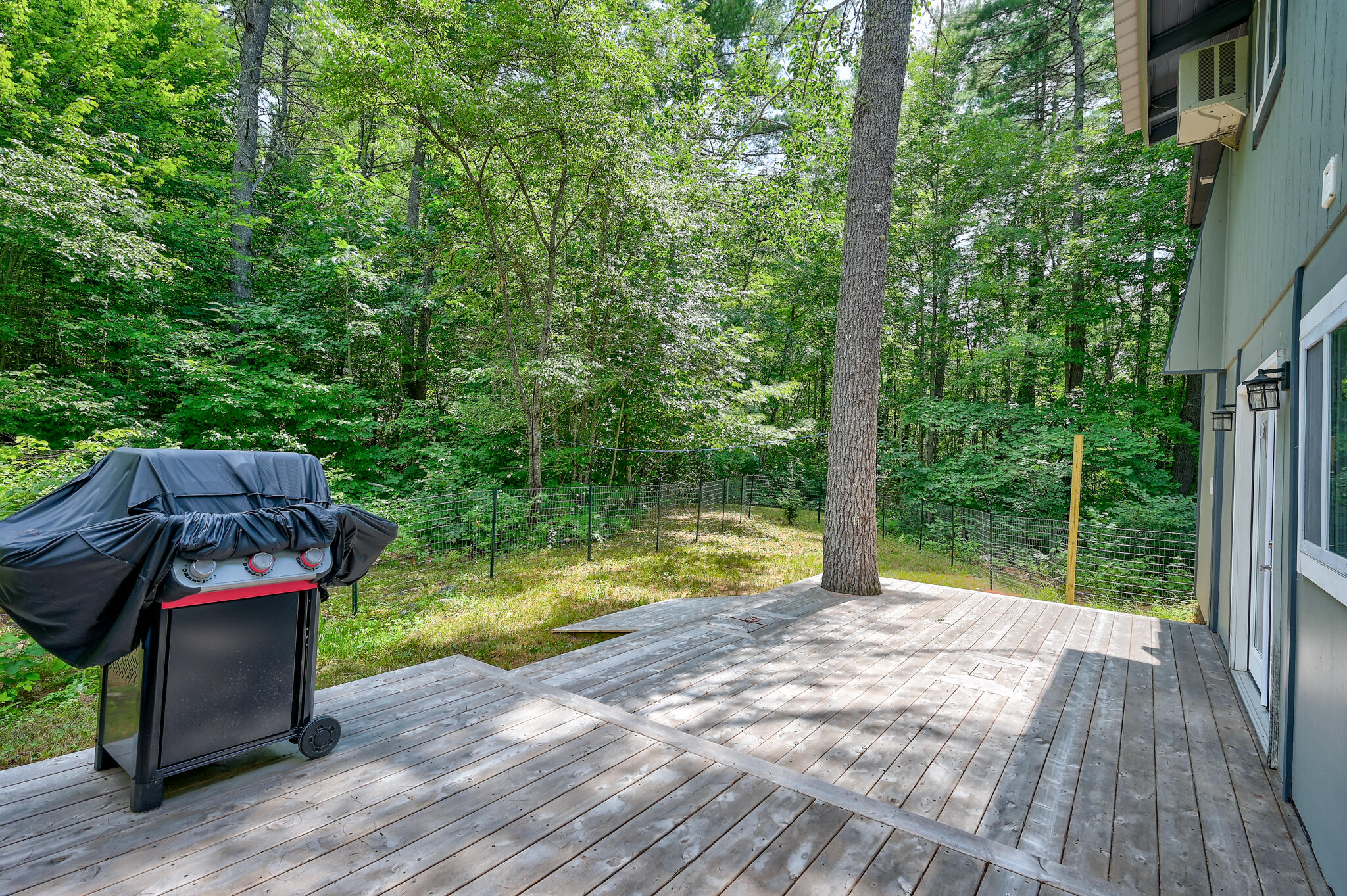 Wooden deck beside a wooded yard, with a covered grill and wire fencing.