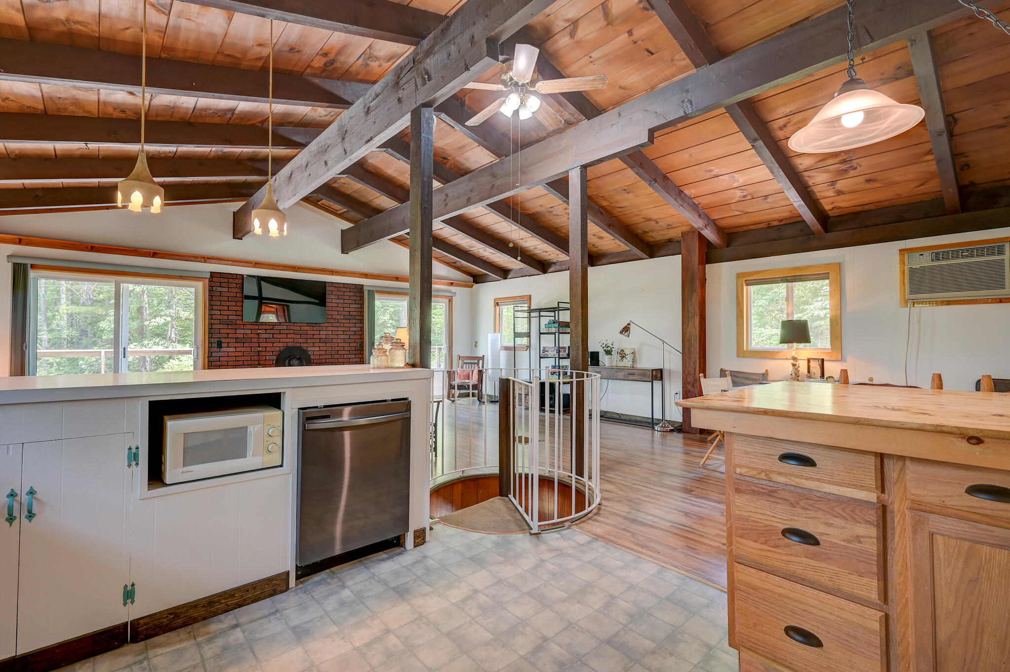 Open kitchen and dining area with exposed timber beams, a brick fireplace, and wood cabinetry.