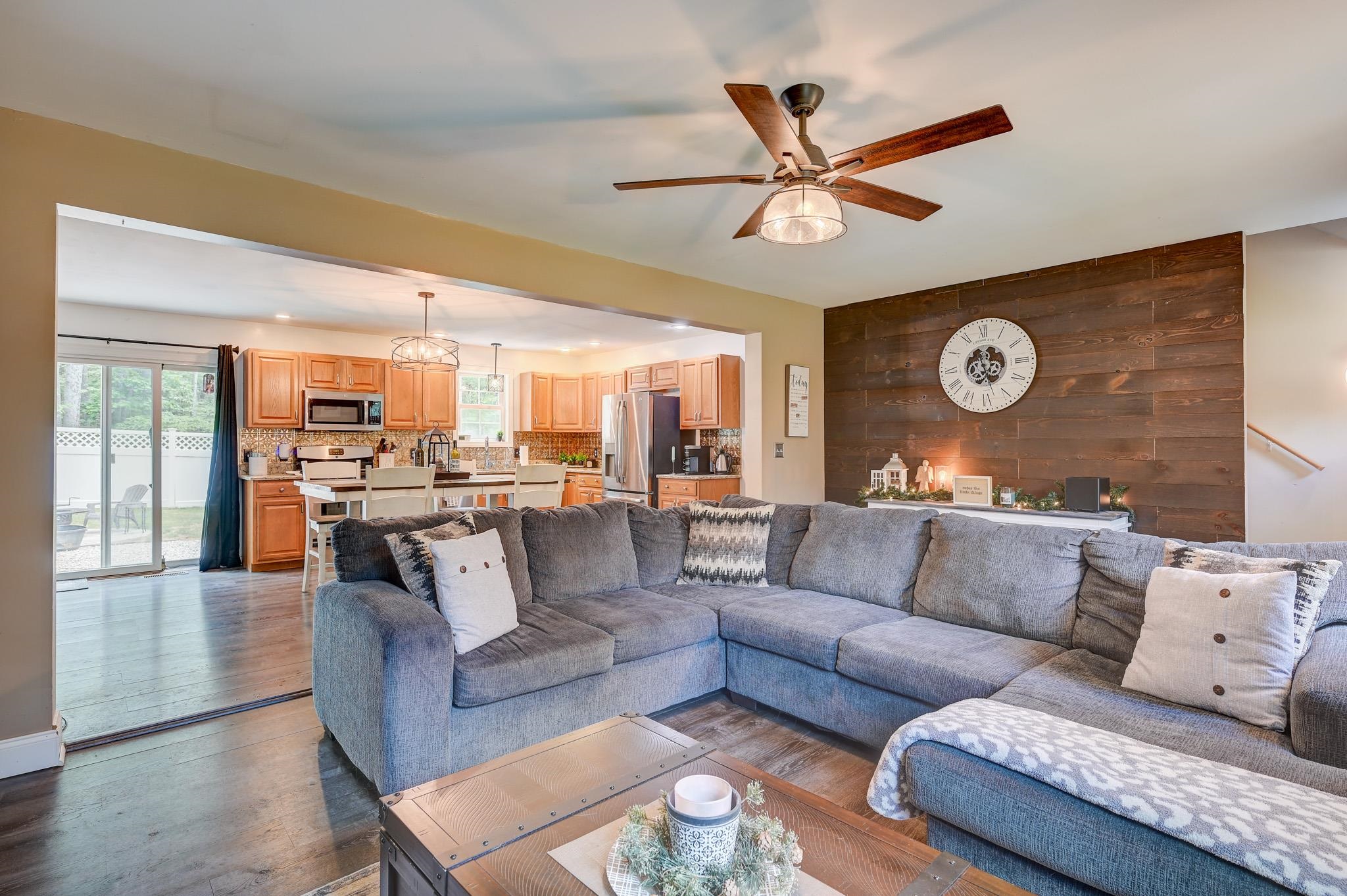 Open-plan living room and kitchen with a gray sectional, dark wood accent wall, and warm wood cabinets.