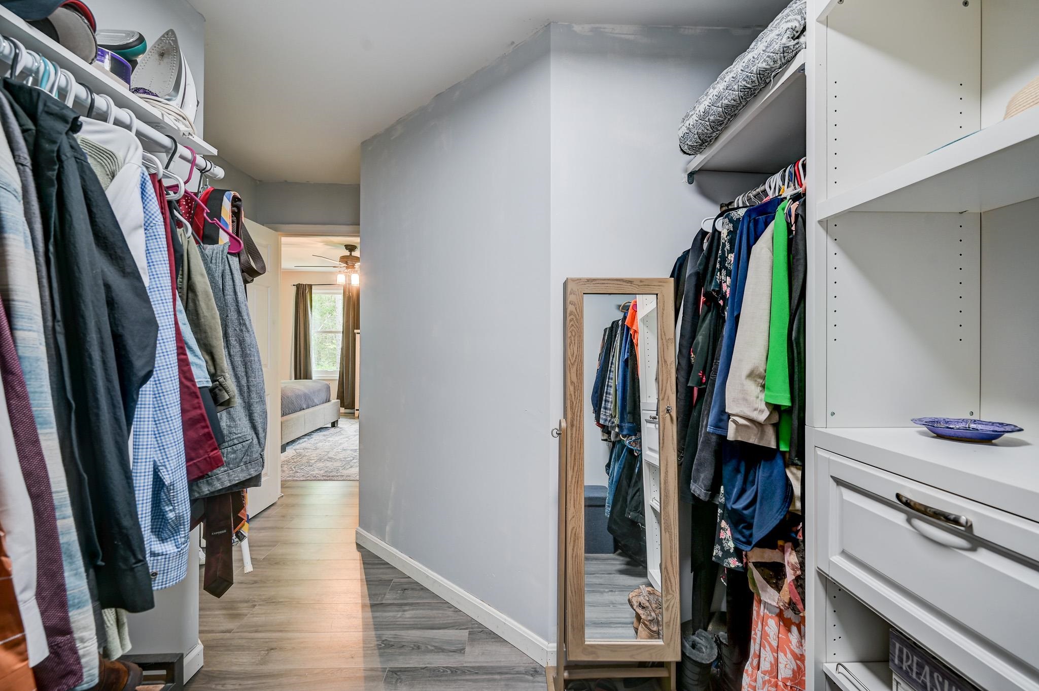 Walk-in closet with clothes on both sides, built-in shelving, and a full-length mirror.