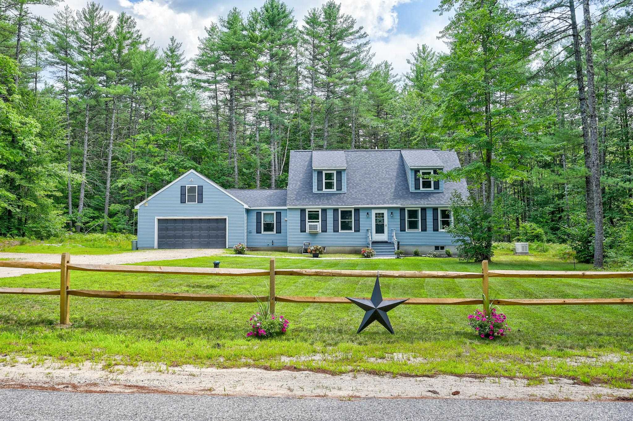 Light blue house with an attached garage behind a split-rail fence, surrounded by trees.