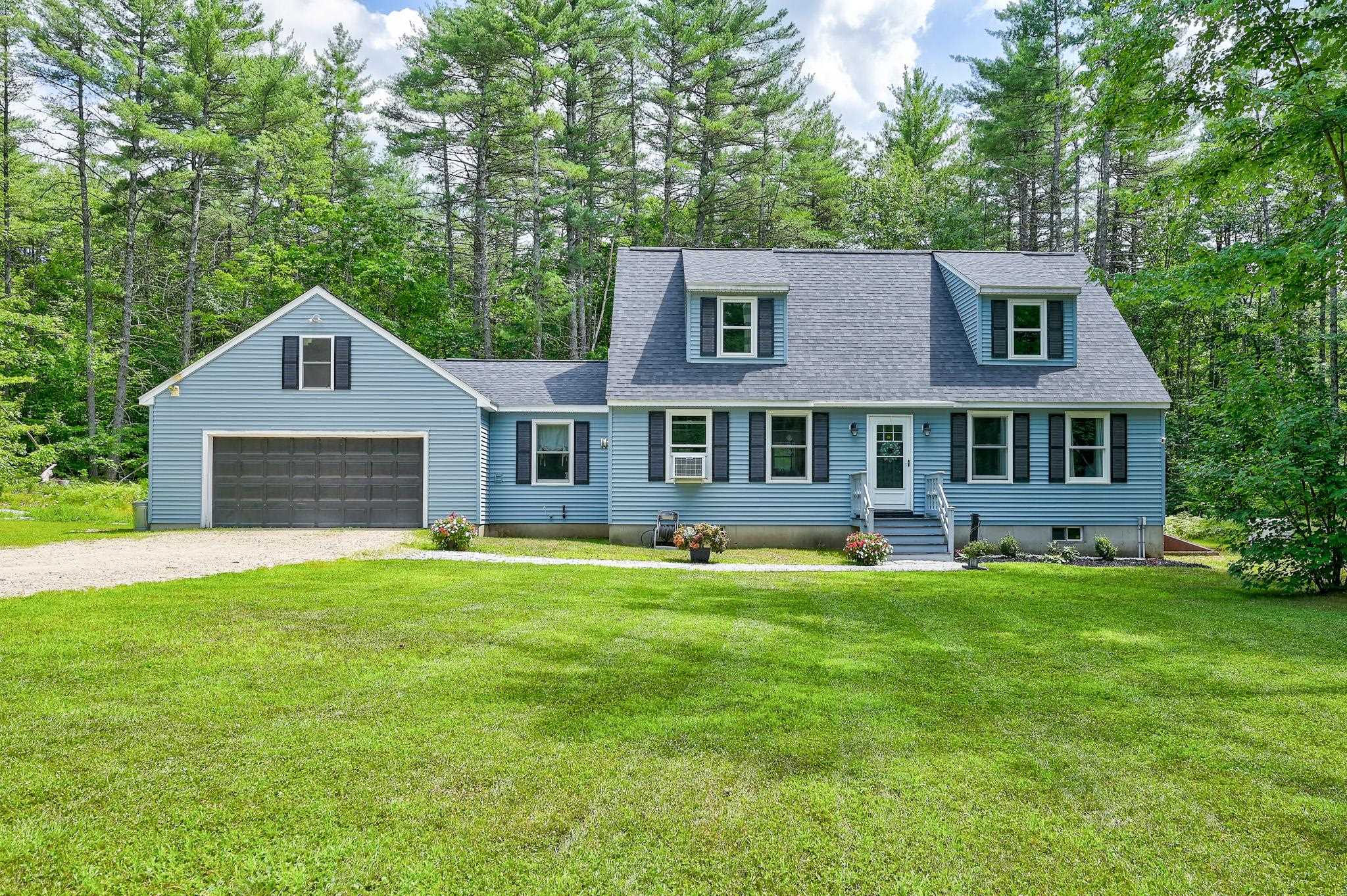 Blue house with attached garage and dormers, set behind a broad lawn among mature trees.