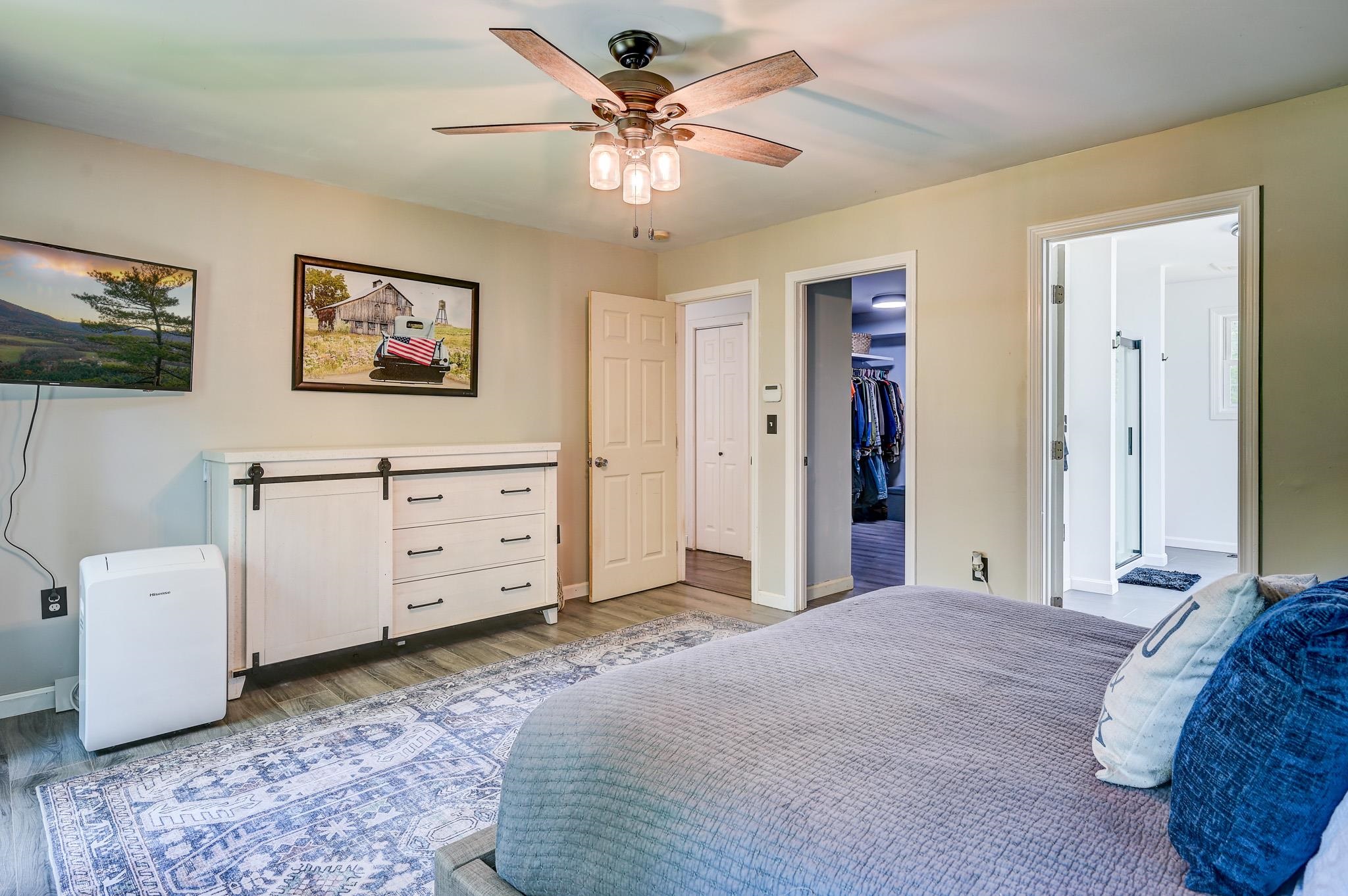 Bedroom with a gray quilted bed, patterned rug, and doorways to a closet and bright bathroom.