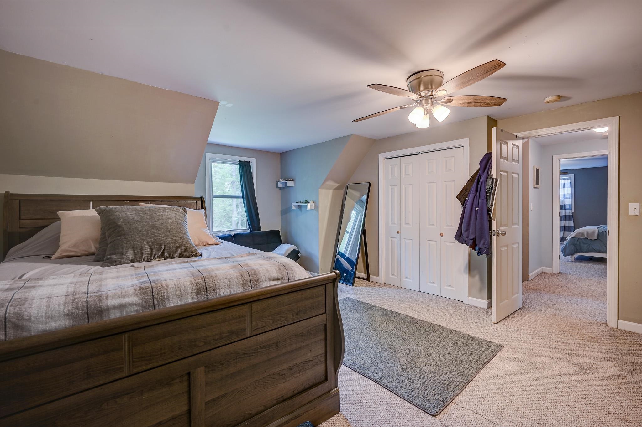 Furnished bedroom with a large wood bed, sloped ceiling, and ceiling fan.