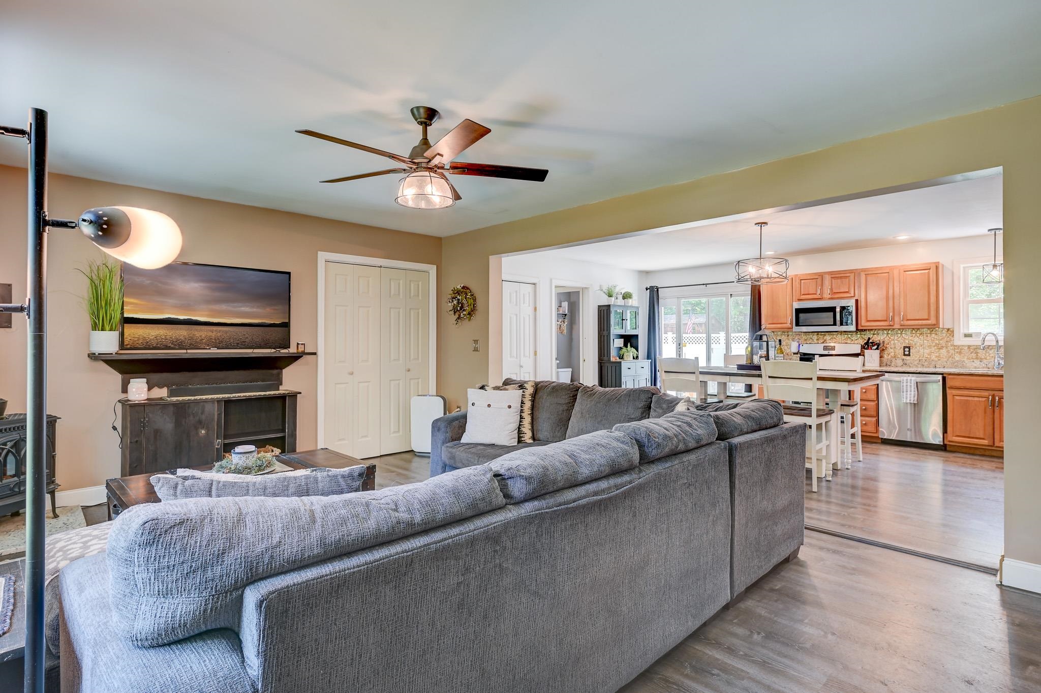 Open-plan living room and kitchen with a gray sectional, wood cabinets, and a breakfast bar.