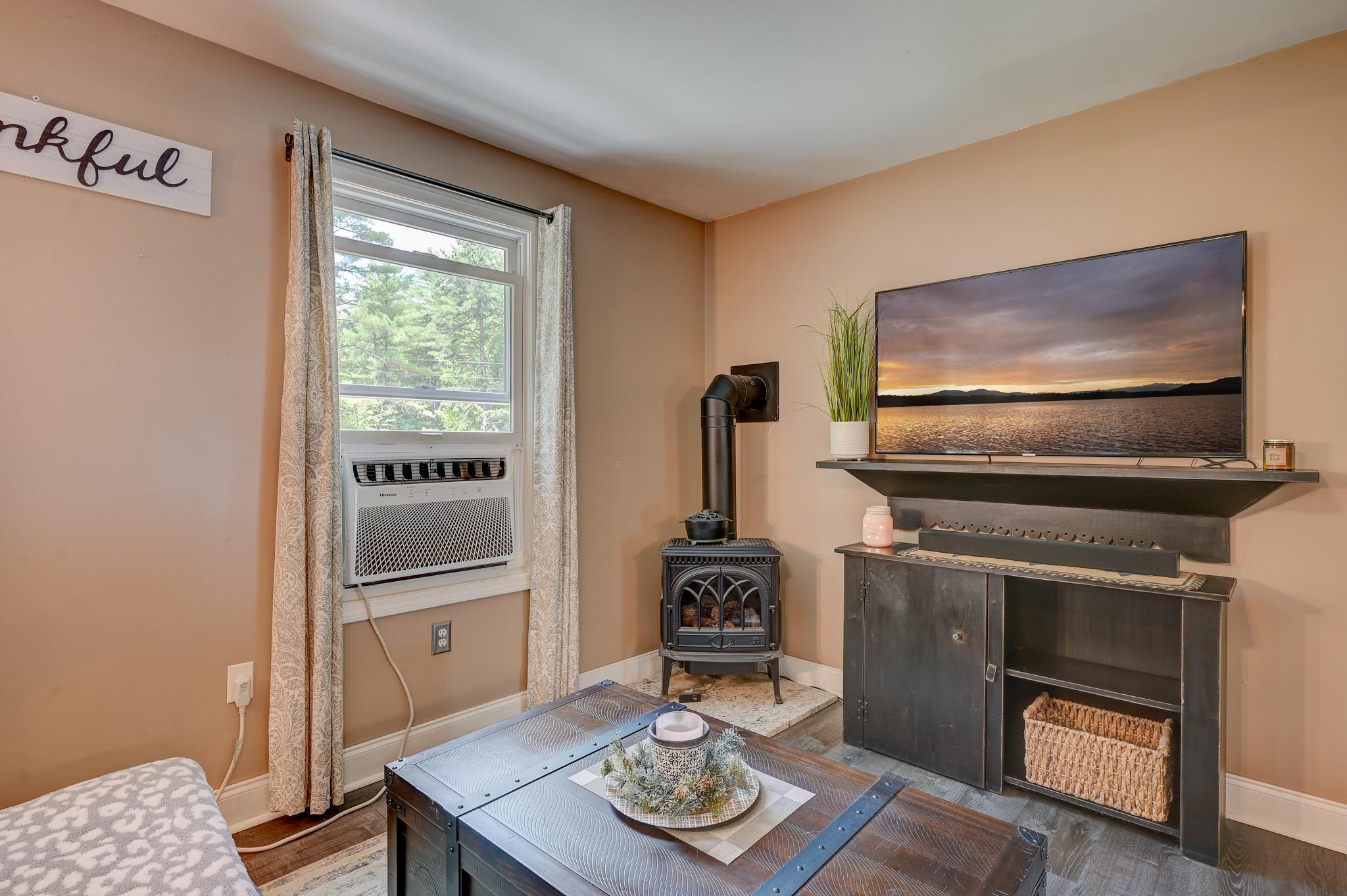 Living room with a freestanding wood stove, window air conditioner, and dark media console.
