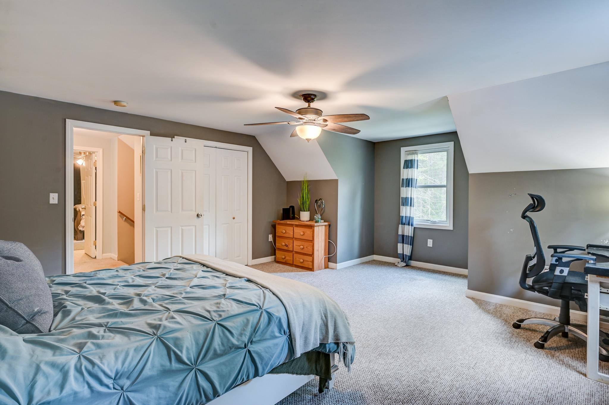 Bedroom with blue bedding, sloped ceiling, ceiling fan, and a desk beside the window.