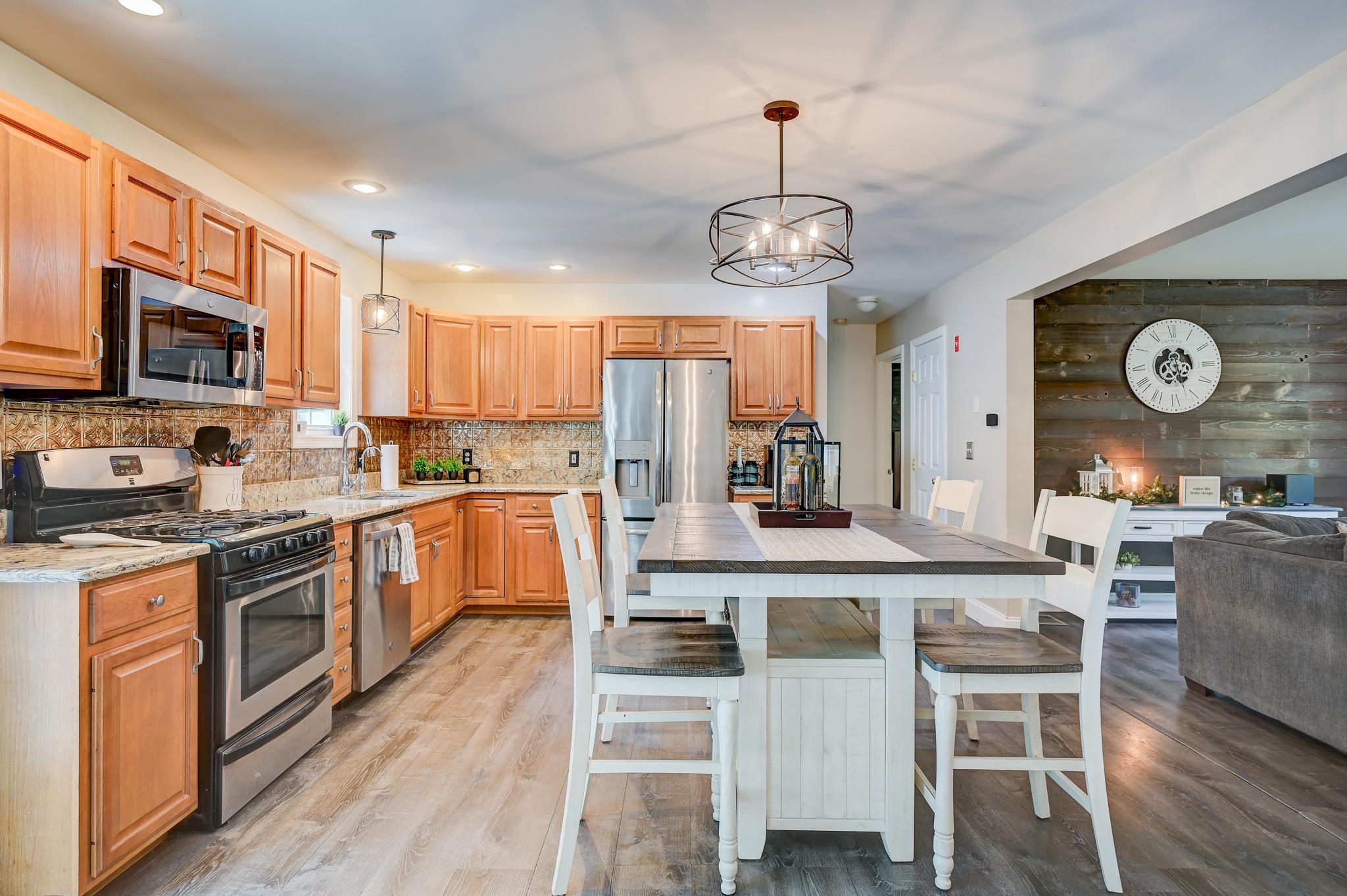 Open kitchen and dining area with warm wood cabinets, stainless steel appliances, and a large white table.