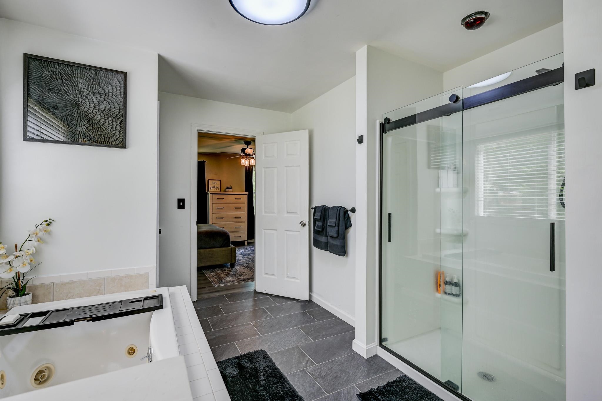 Bathroom with a glass walk-in shower, jetted tub, and gray tile floor.