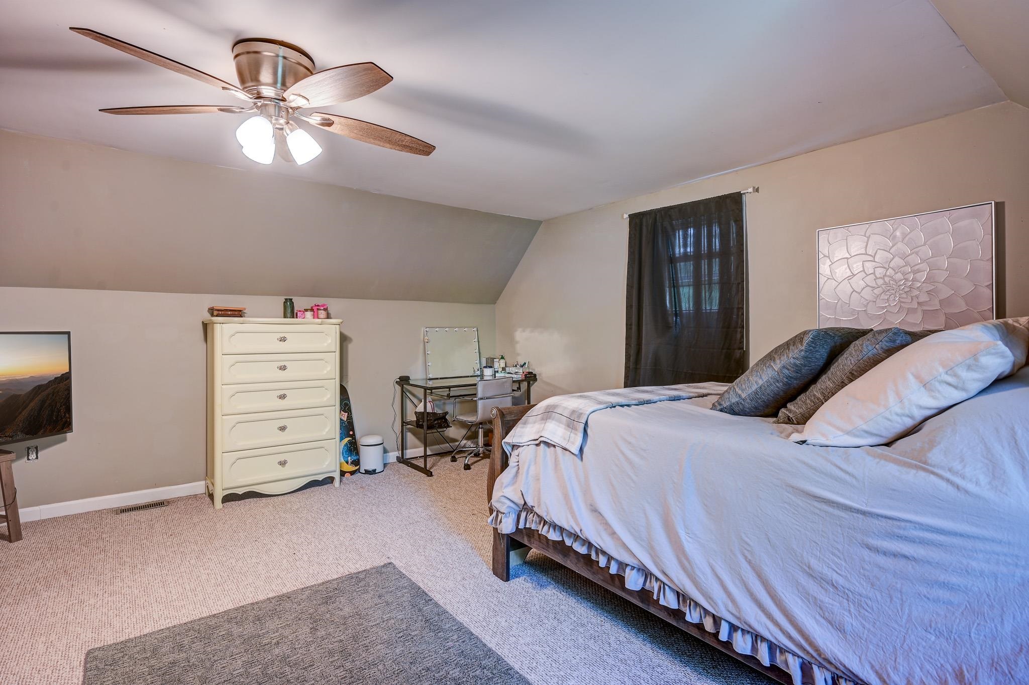 Furnished bedroom with a large bed beneath a sloped ceiling and a ceiling fan.