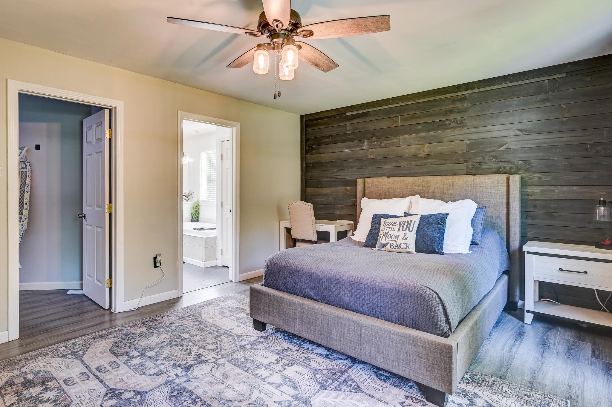Bedroom with a gray upholstered bed, dark wood-plank accent wall, and patterned rug.