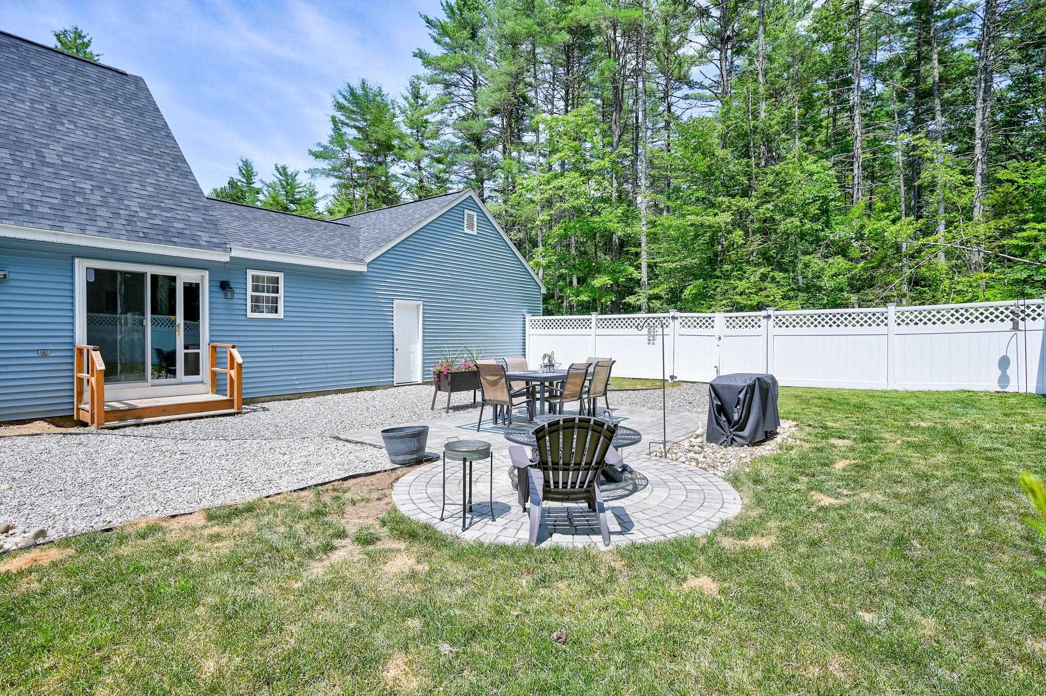 Blue-sided house and fenced backyard with gravel patio, outdoor dining set, and circular paver seating area.