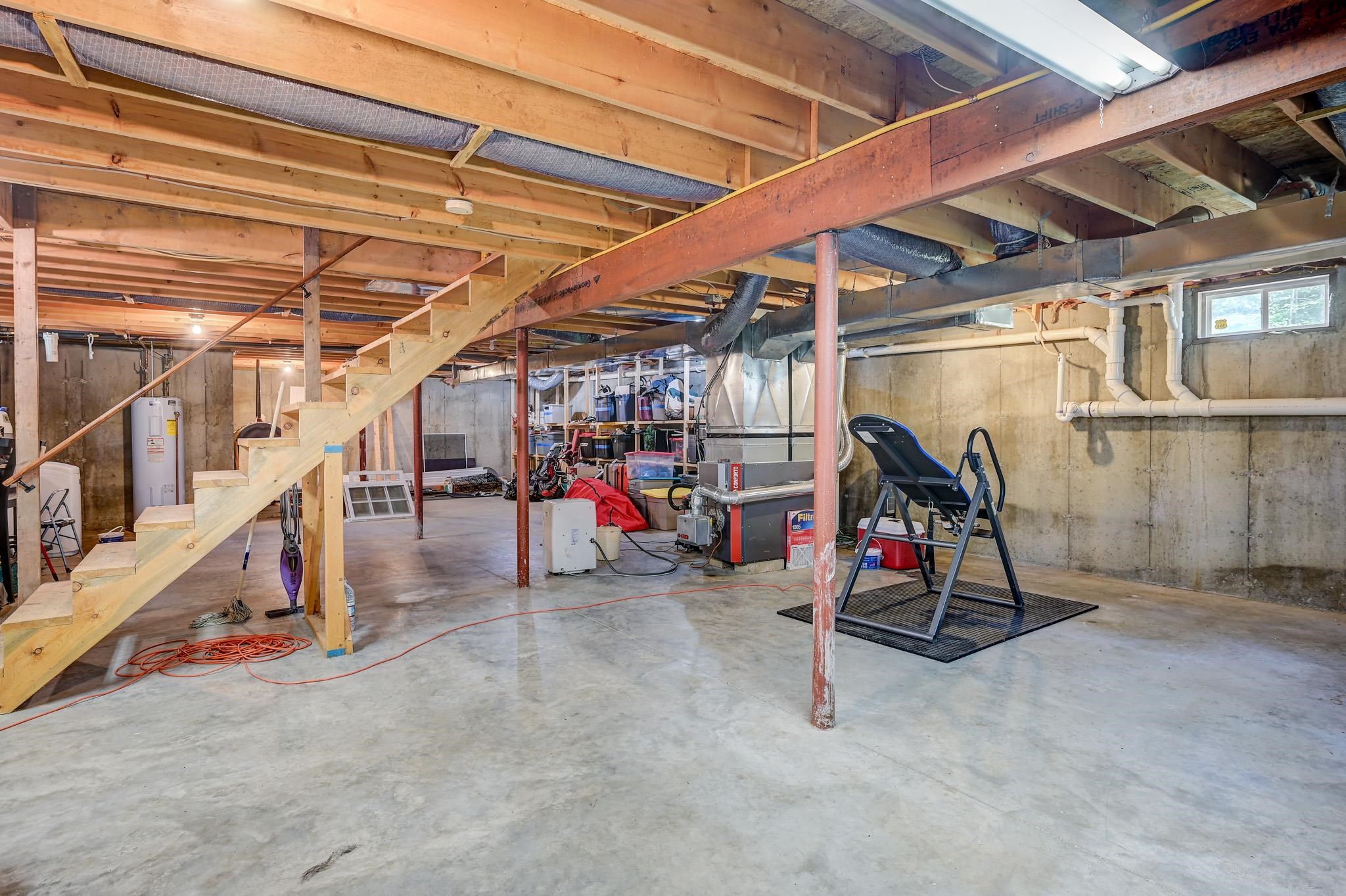 Unfinished basement with exposed framing, wooden stairs, concrete floor, and heating equipment.