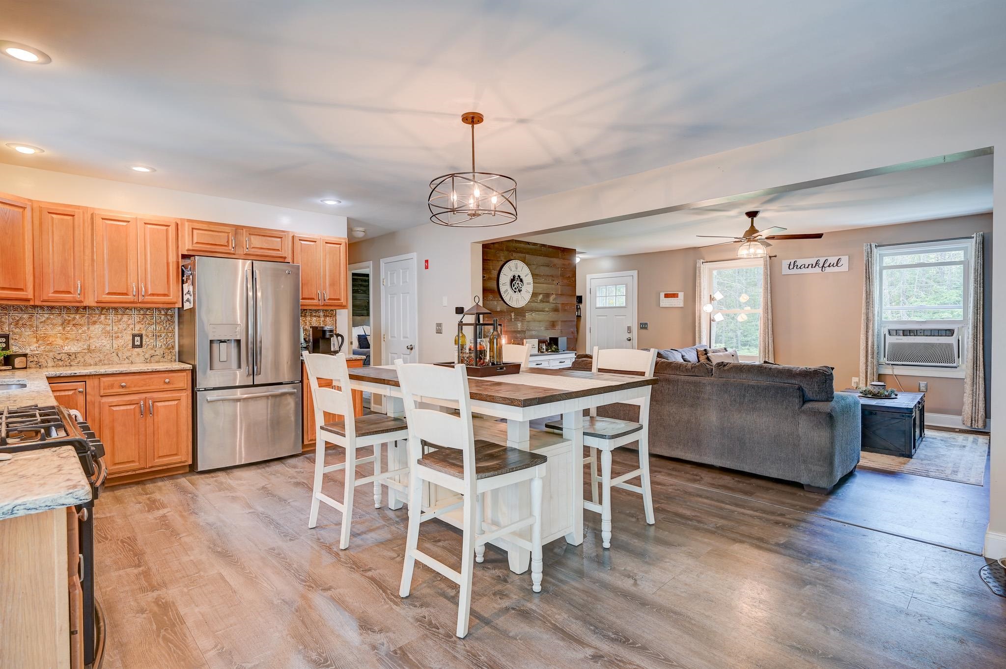 Open-plan kitchen and living room with warm wood cabinets, stainless steel appliances, and a white dining table.