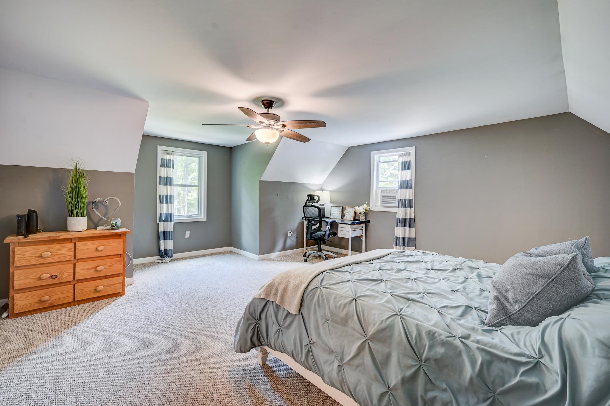 Attic bedroom with a pale blue-gray bed, sloped ceilings, and a small desk beneath a window.
