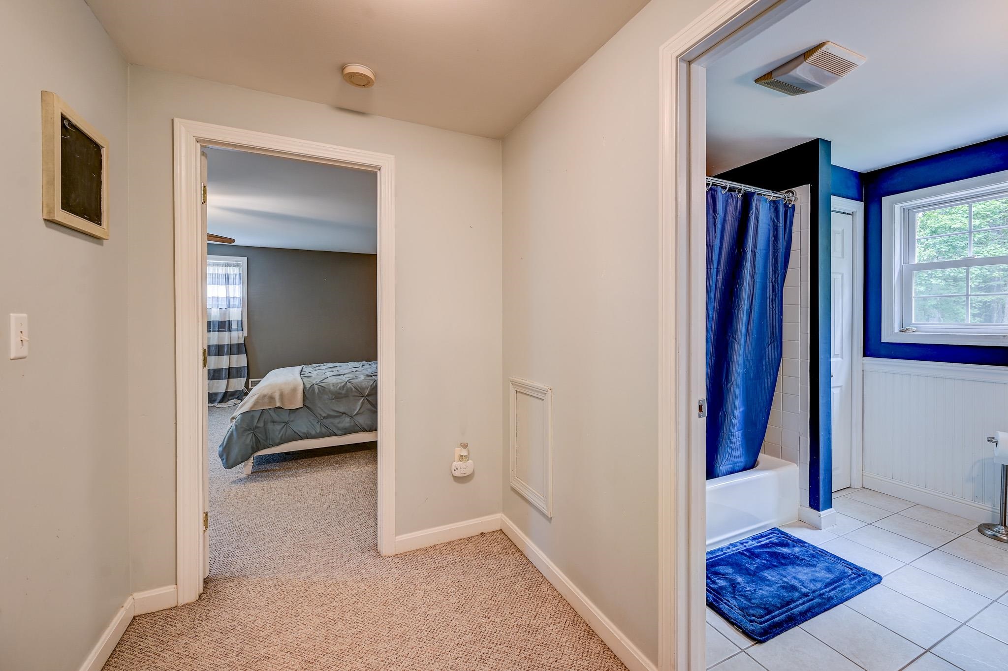 Carpeted hallway between a bedroom and a bathroom with a blue shower curtain and tiled floor.