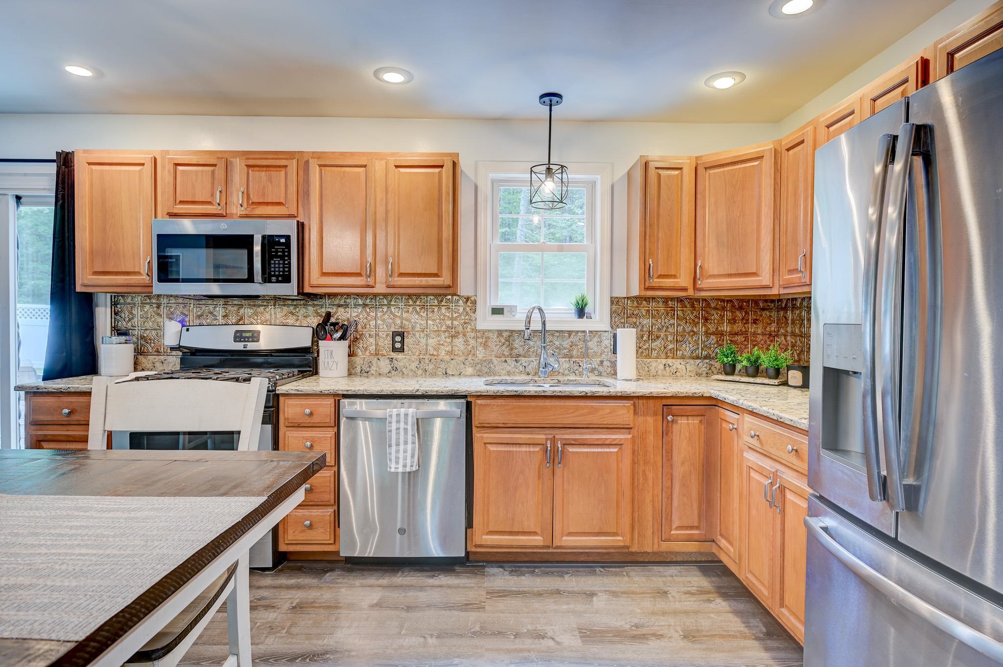 Kitchen with honey-colored cabinets, patterned tile backsplash, granite counters, and stainless steel appliances.