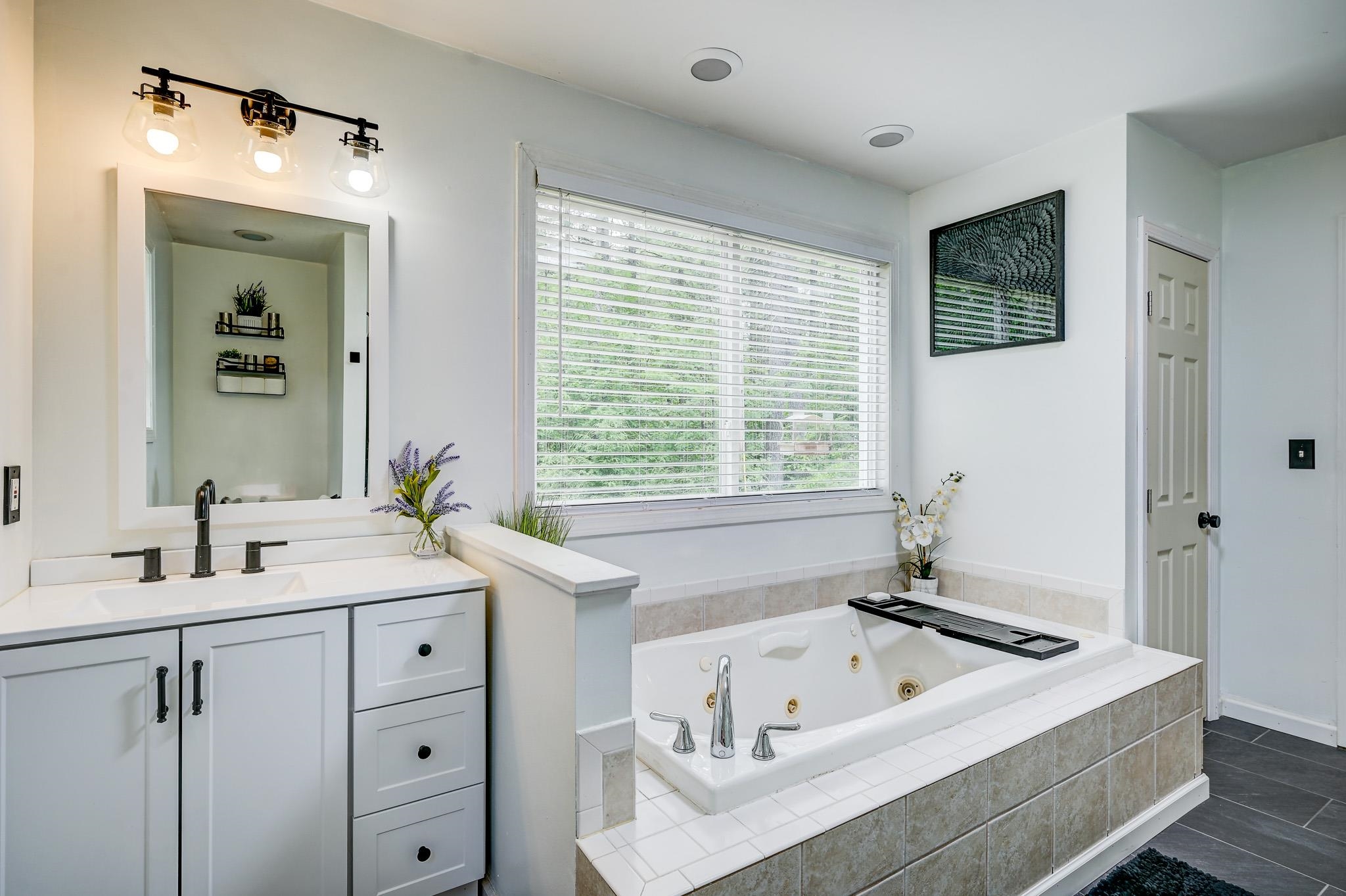 Bright bathroom with a built-in jetted soaking tub beneath a wide window and a white vanity.