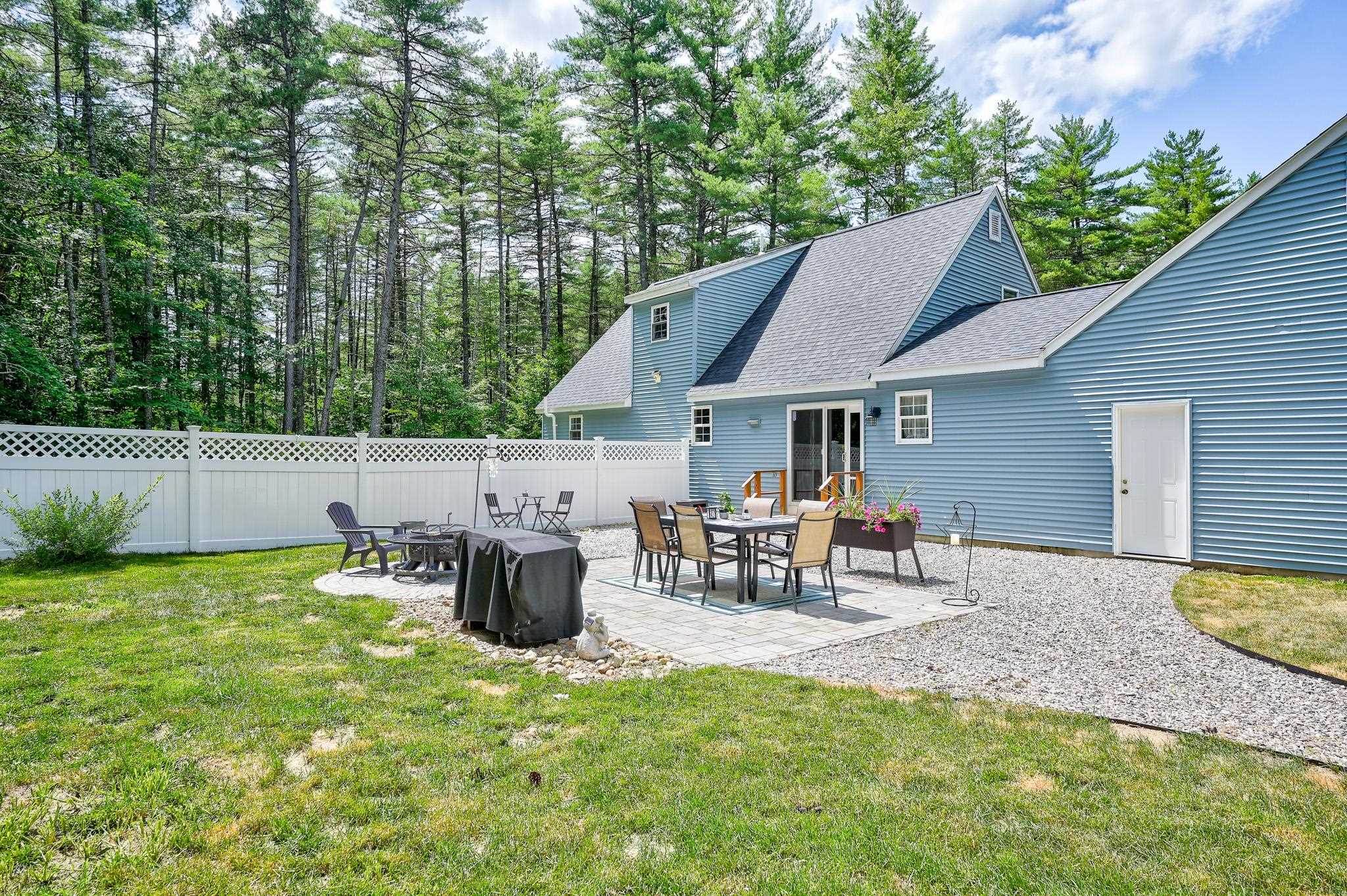 Blue house with a furnished stone patio, white fence, and wooded surroundings.