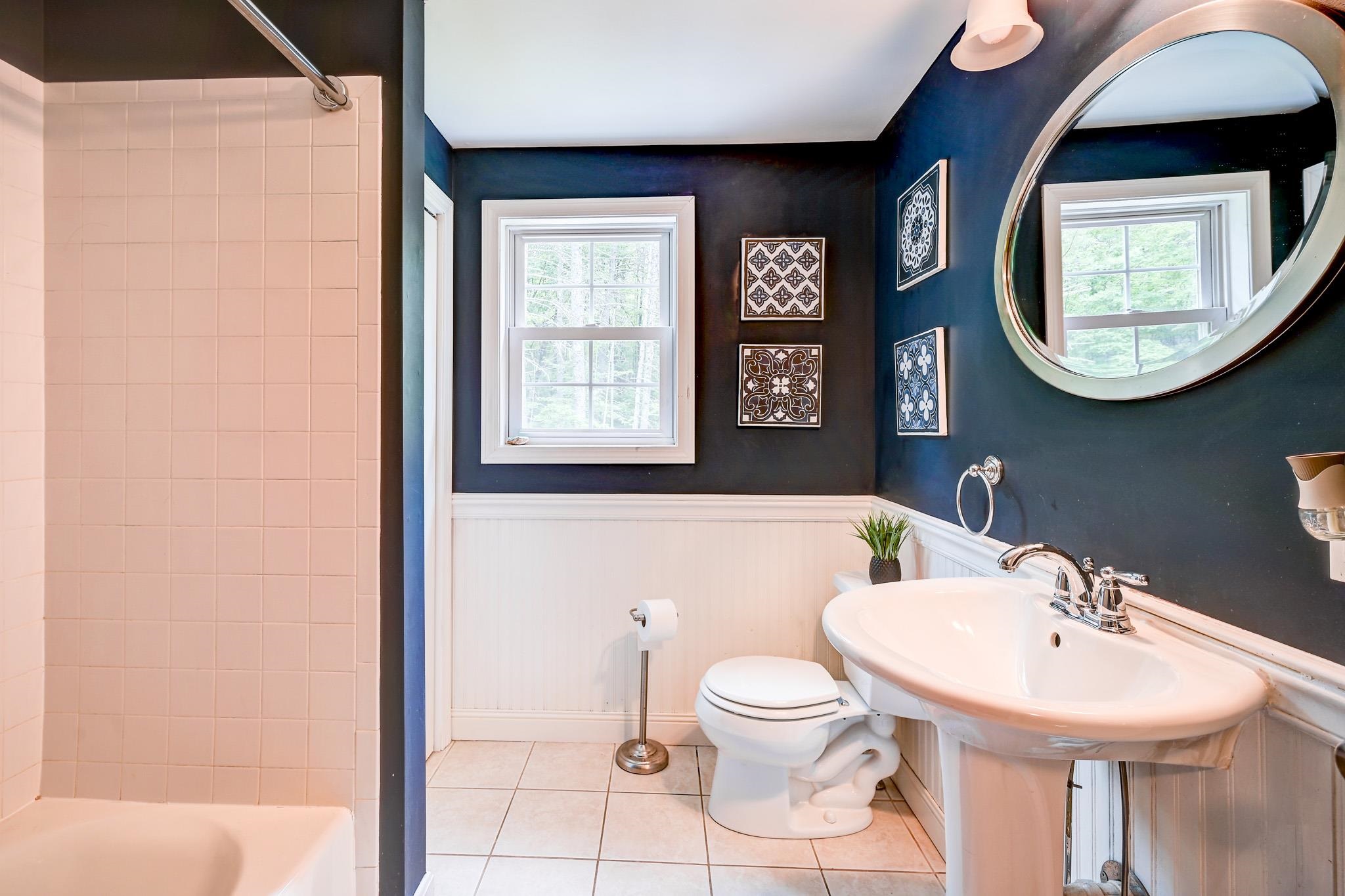 Bathroom with a tiled shower, pedestal sink, and large round mirror against dark blue walls.