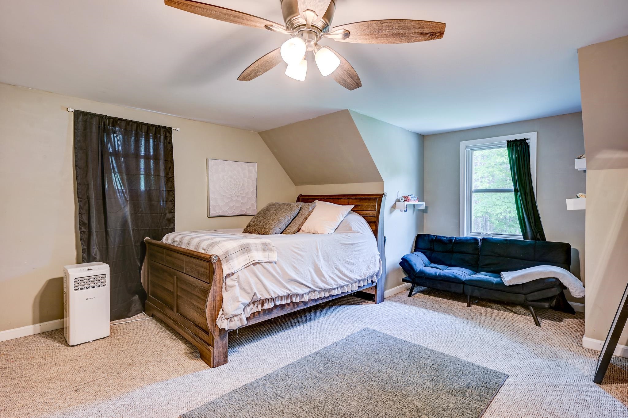 Bedroom with a wooden bed, dark sofa beside a window, and ceiling fan.