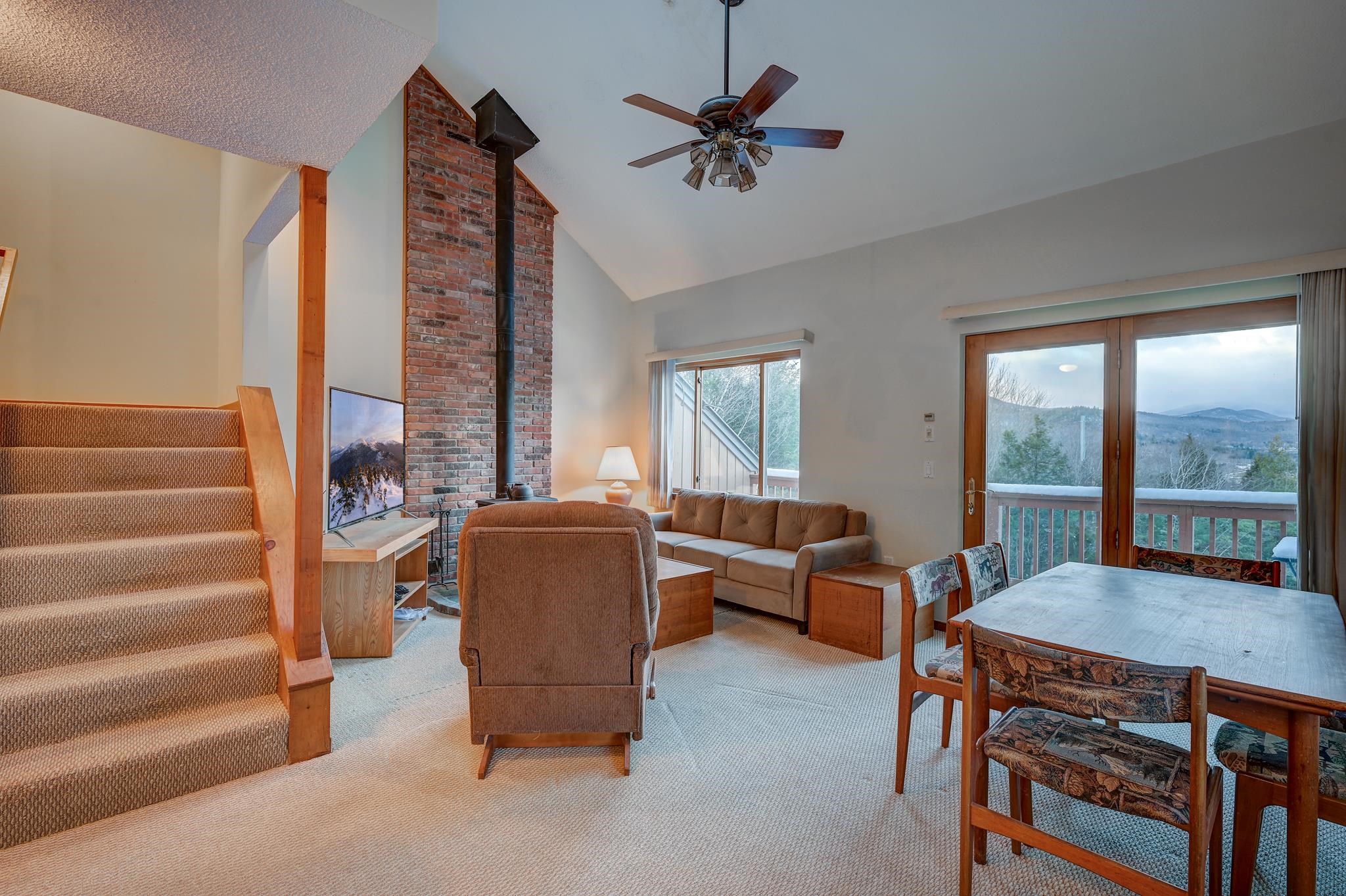 Living and dining area with a brick chimney, carpeted stairs, and mountain views through glass doors.