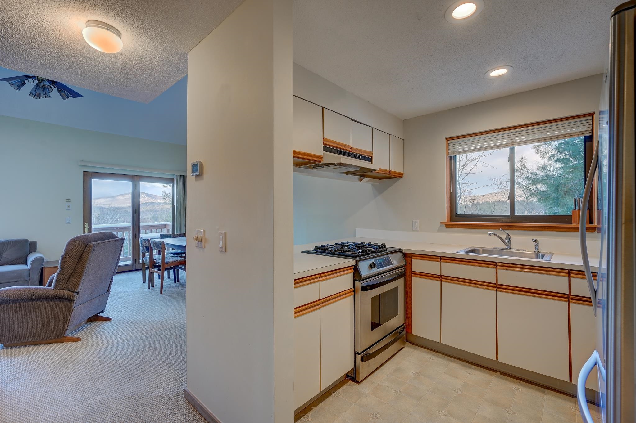 Kitchen with wood-trimmed white cabinets and mountain views, opening onto a furnished living and dining area.