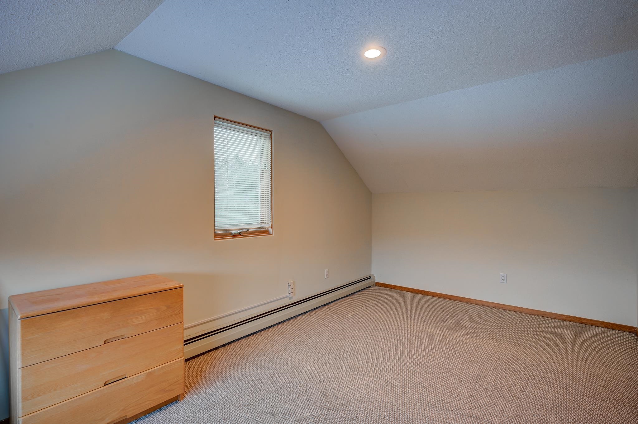Attic bedroom with a sloped ceiling, carpet, a narrow window, and a wooden dresser.