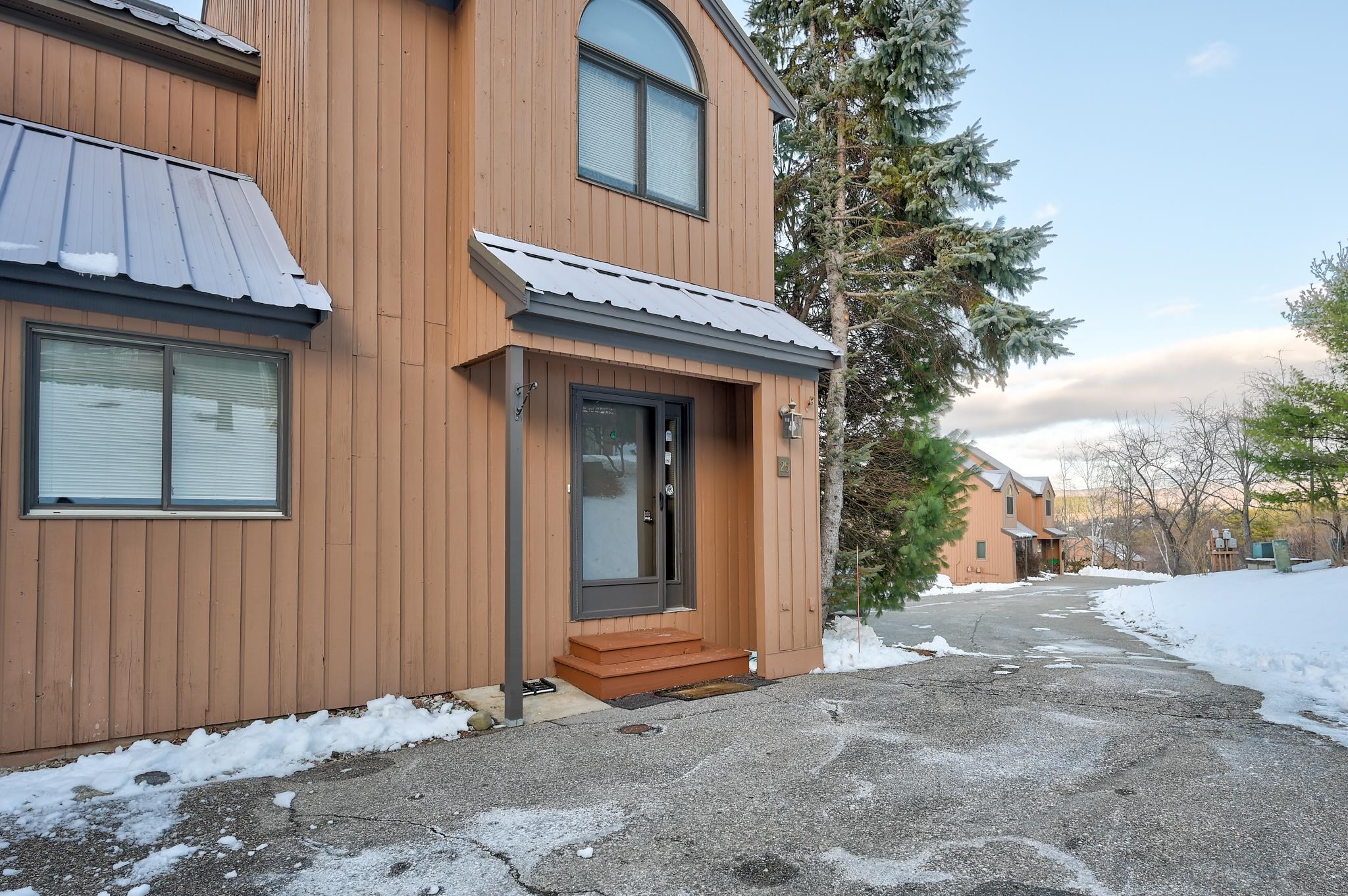Brown townhouse entrance with gray metal awning and snow along the driveway.