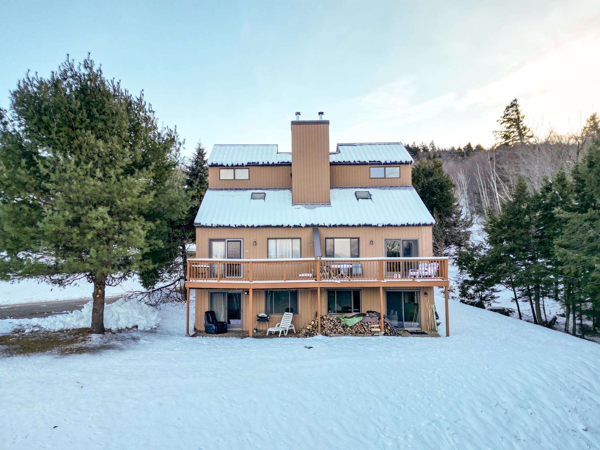 Rear of a brown multi-level home with a wooden deck and snow-covered roof.