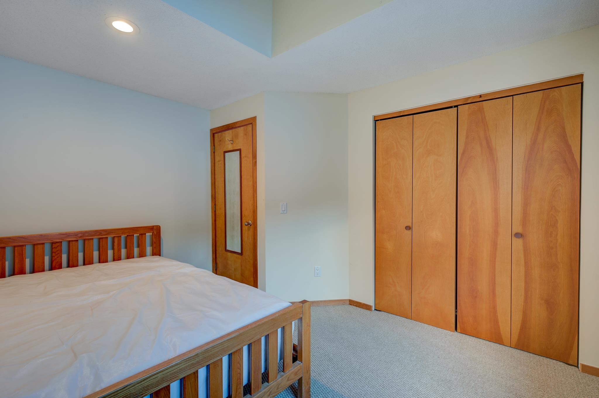 Bedroom with a wooden bed, mirrored door, and wide wooden sliding closet doors.
