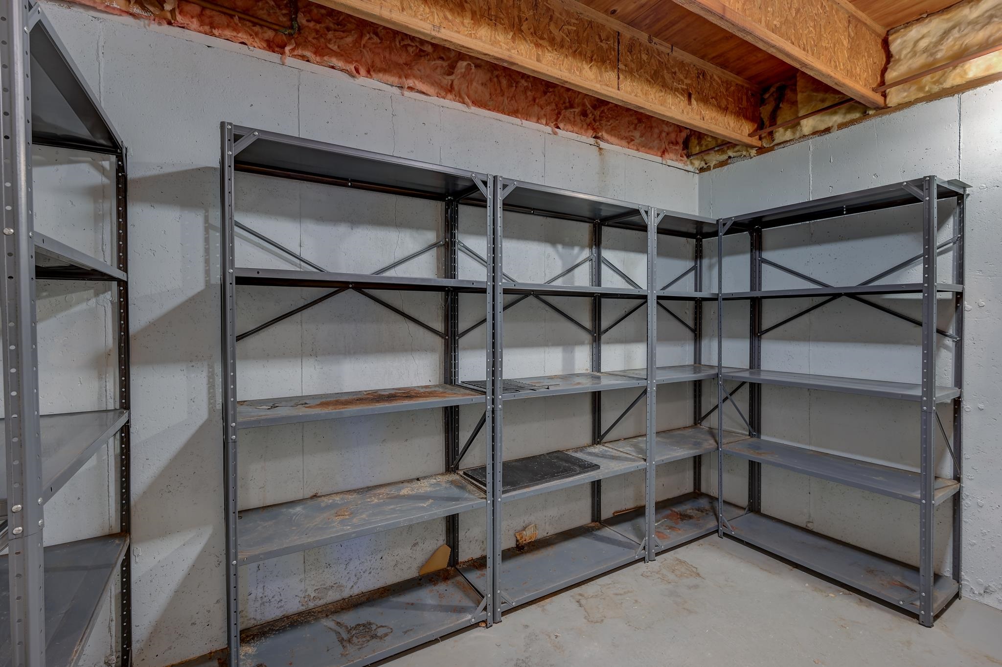 Unfinished basement storage room with metal shelving along three concrete walls and exposed ceiling joists.
