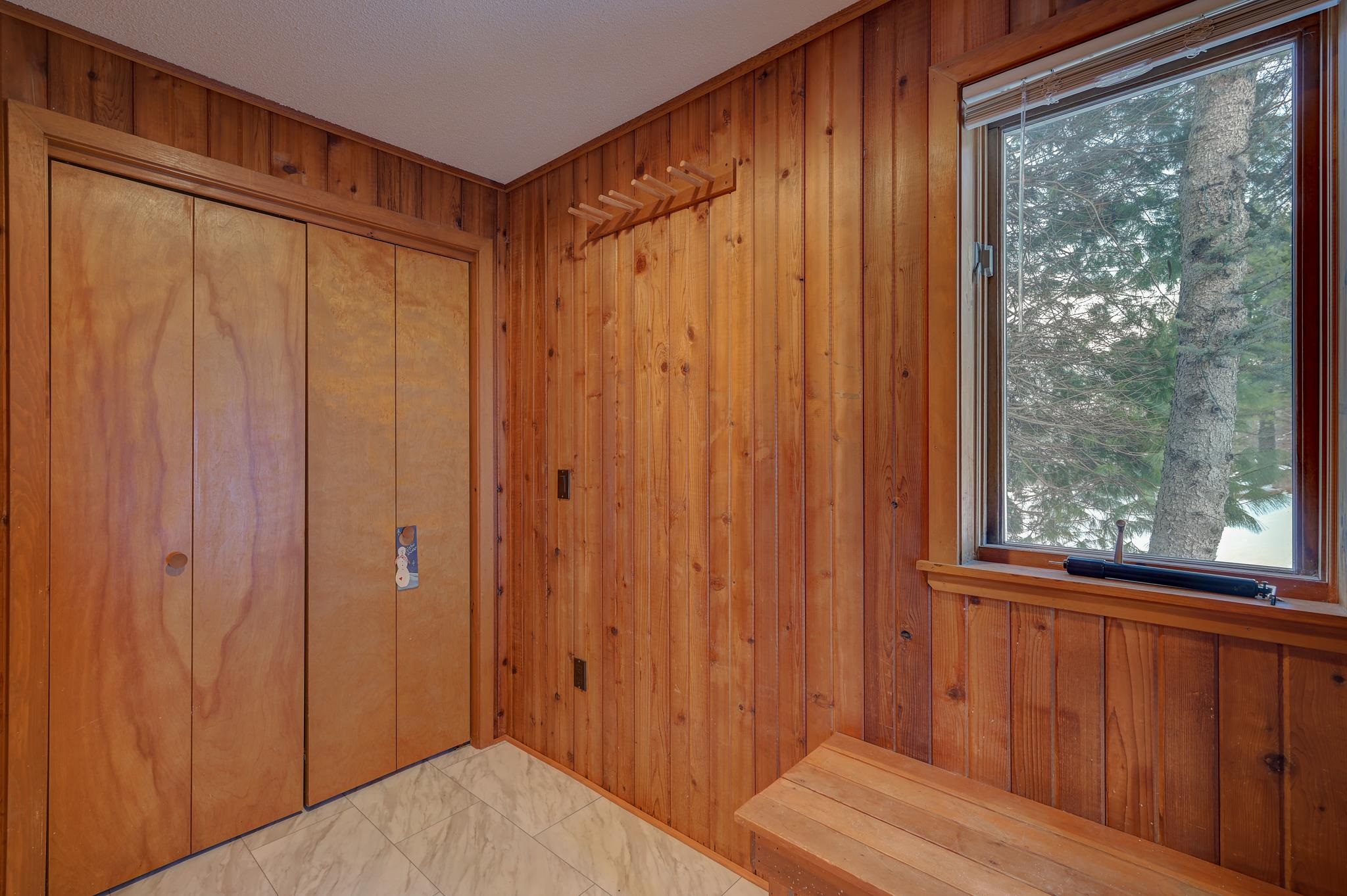 Wood-paneled entryway with sliding closets and a built-in bench beside a window.