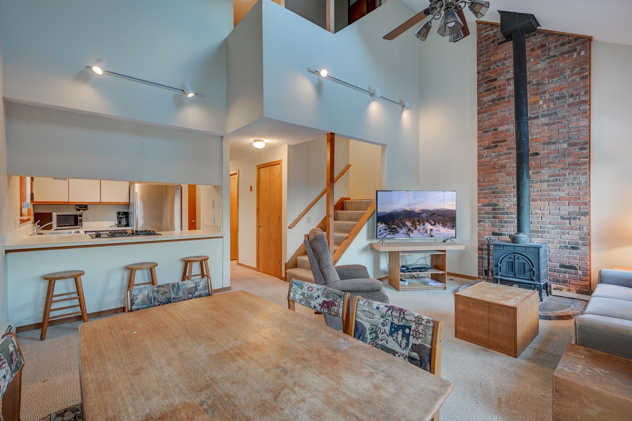 Open-plan living and dining area with a vaulted ceiling, brick fireplace, and kitchen breakfast bar.