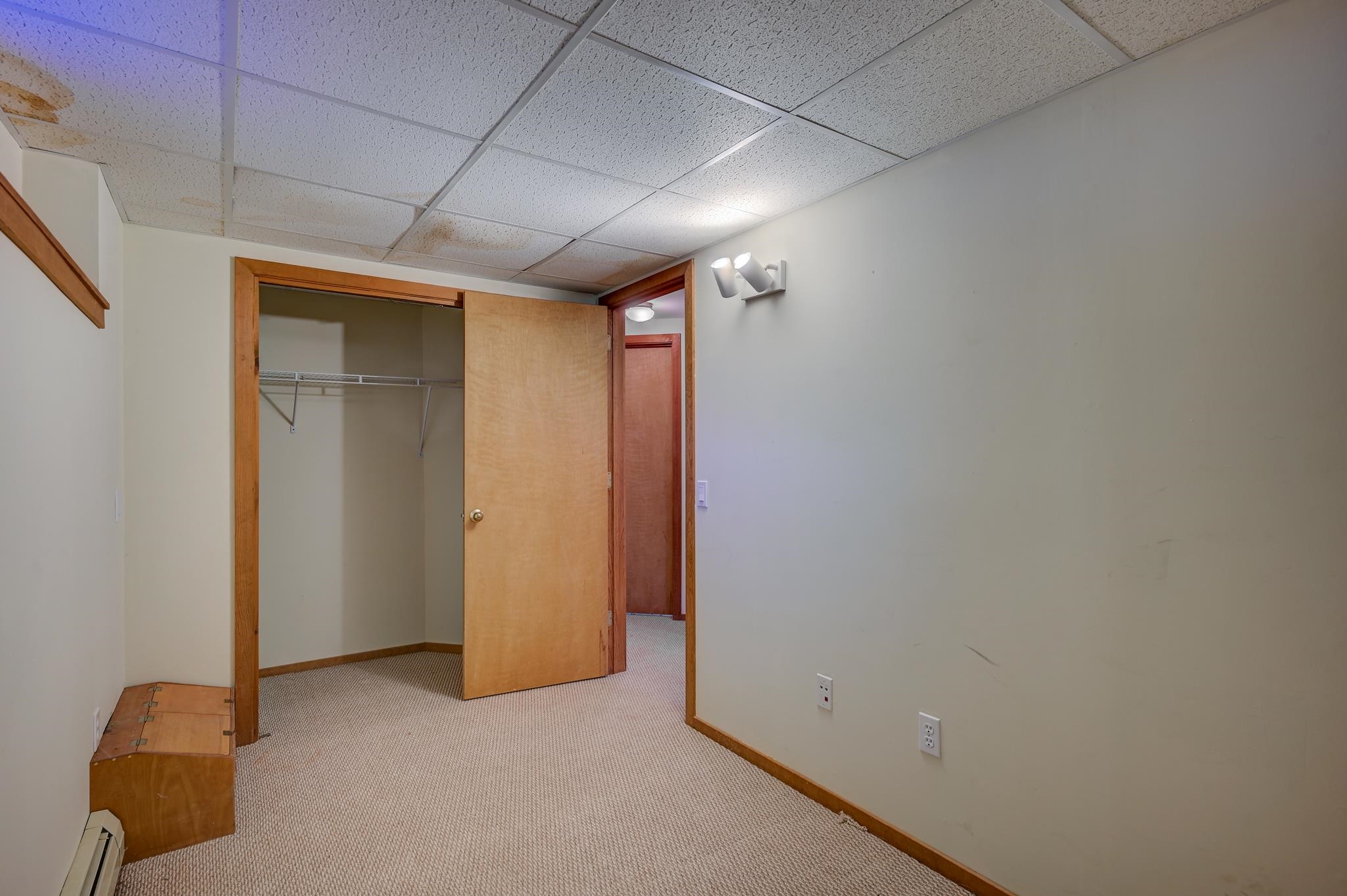 Empty carpeted room with an open closet, wire shelf, and wooden door.