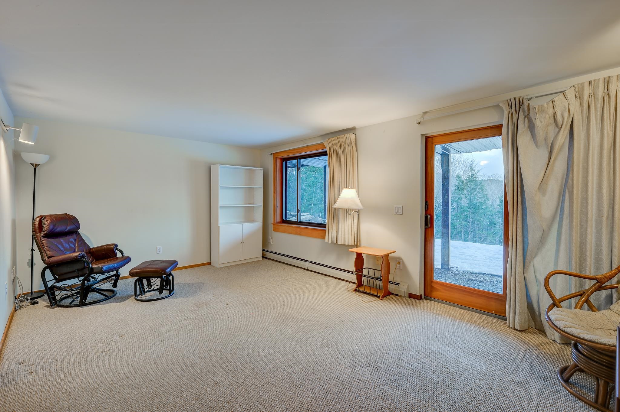 Living room with a leather rocking chair and sliding glass door overlooking snow and trees.