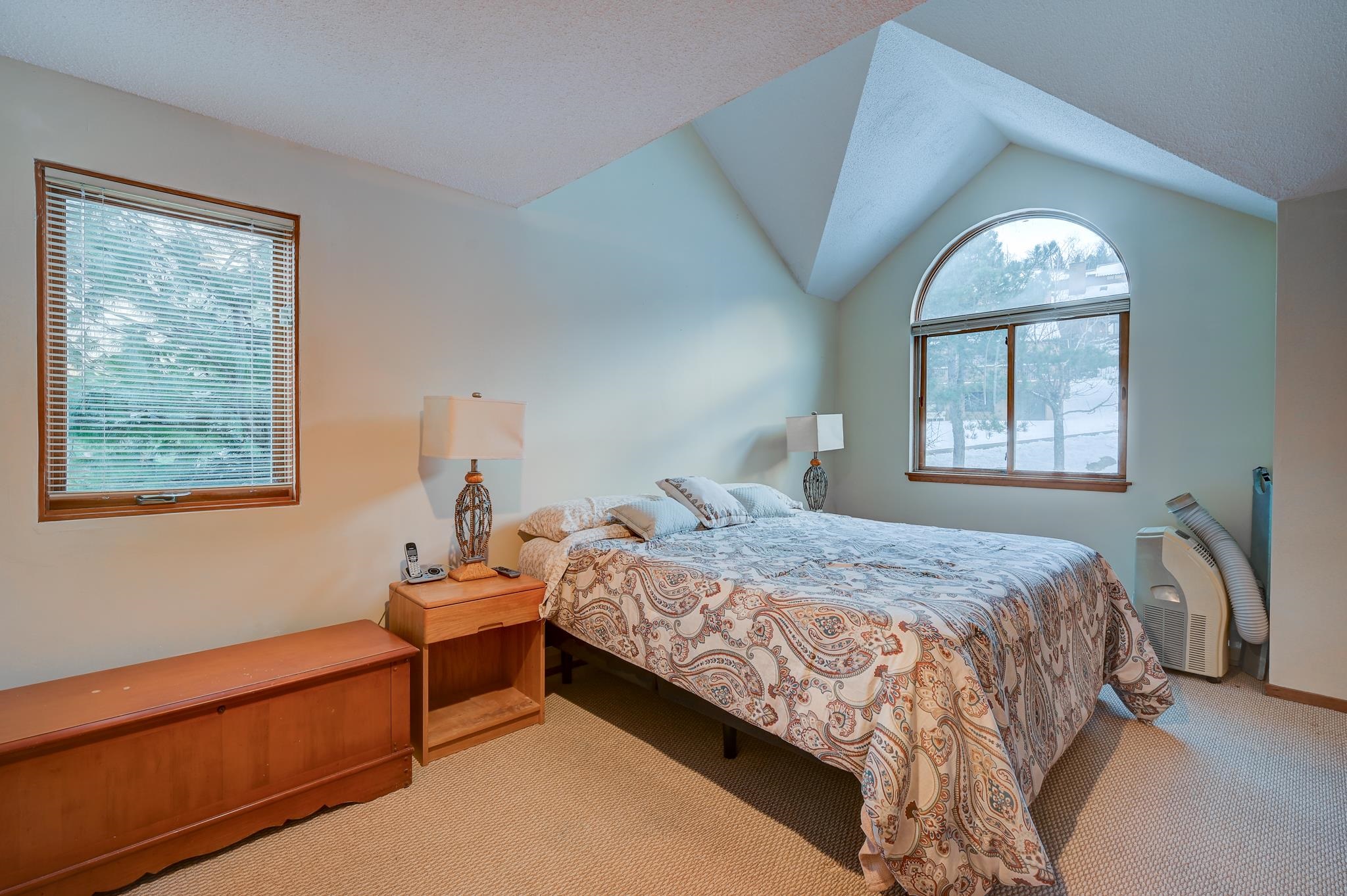 Bedroom with a patterned bedspread, vaulted ceiling, and arched window overlooking snow.