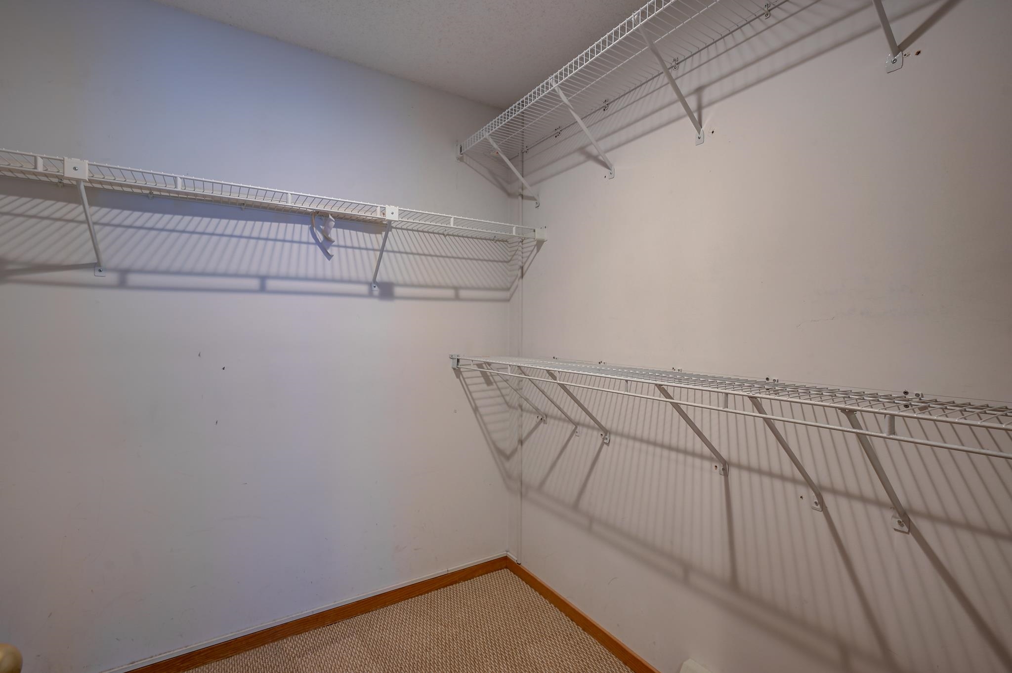 Walk-in closet with white wire shelving on three walls and beige carpet.