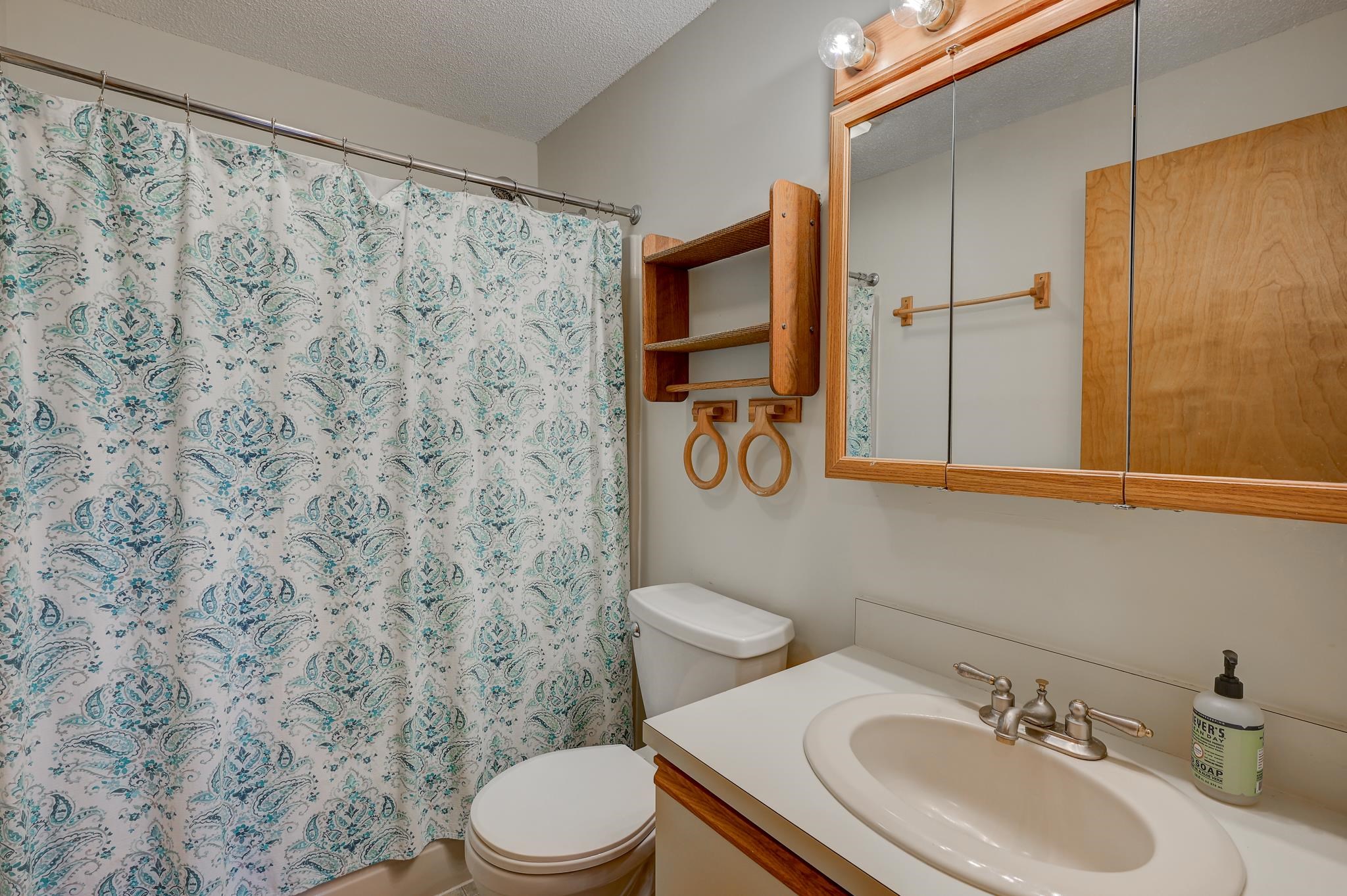 Bathroom with a teal paisley shower curtain and wooden mirrored cabinet above the sink.