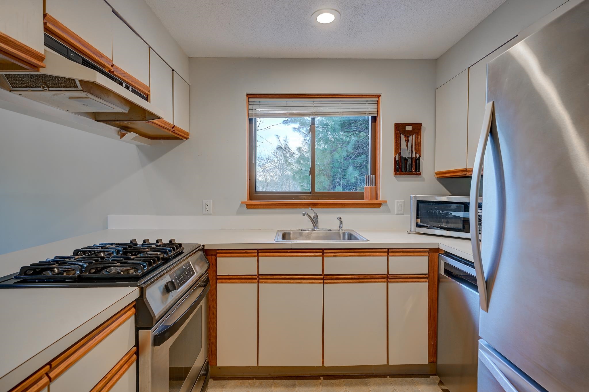 Kitchen with white and wood-trimmed cabinets, gas range, and a window overlooking trees.