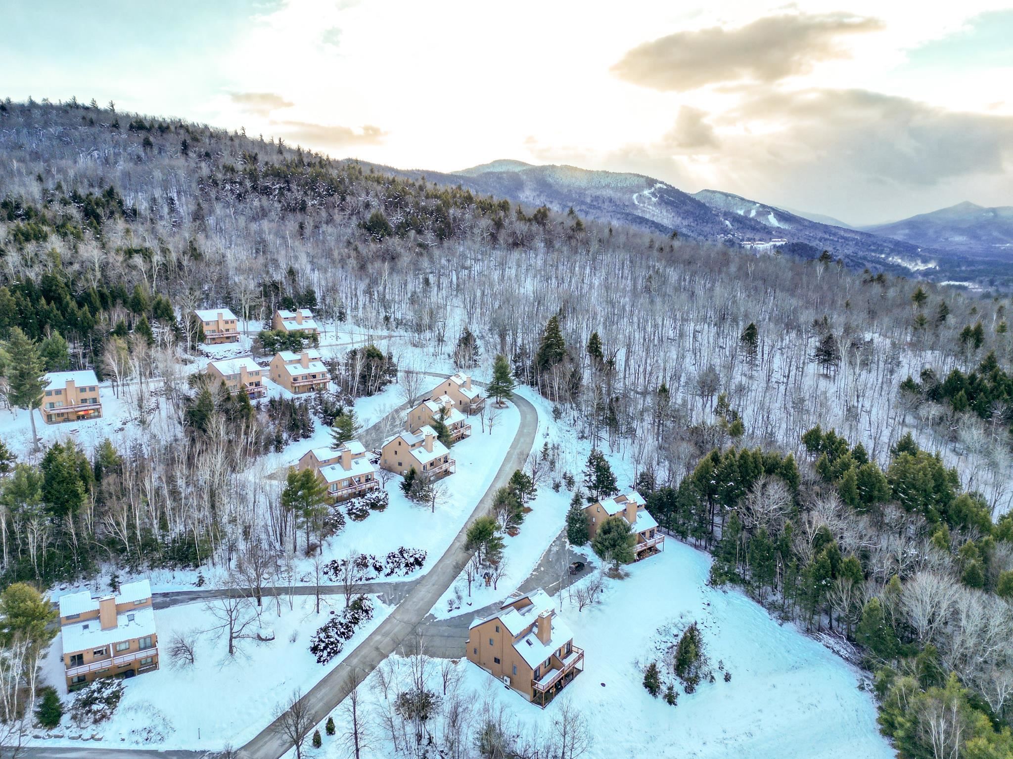 Snow-covered mountain neighborhood with tan homes along a winding road and distant ridges.
