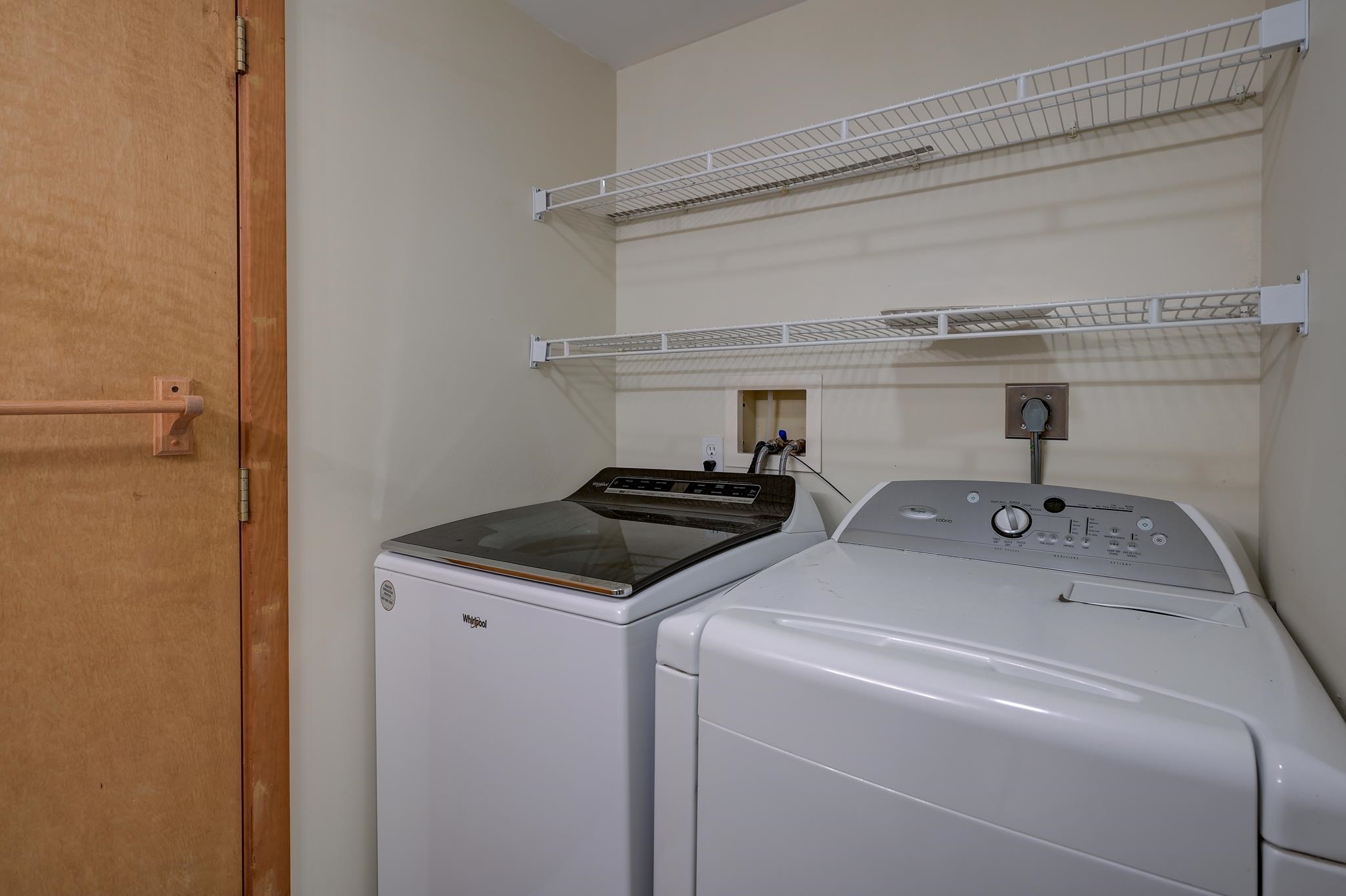 Laundry room with a white washer and dryer beneath two wire storage shelves.