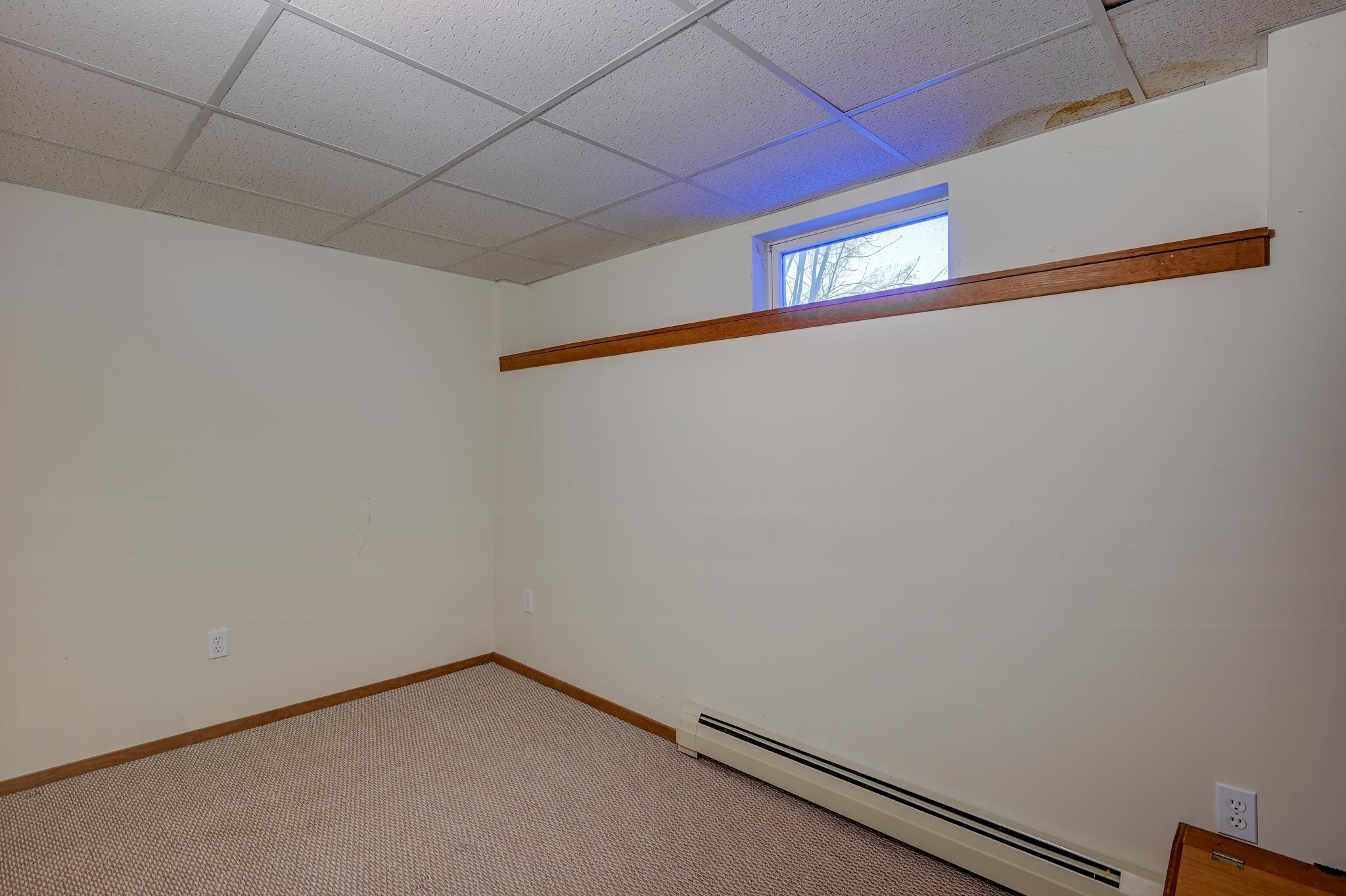 Empty carpeted room with a small high window and baseboard heater.