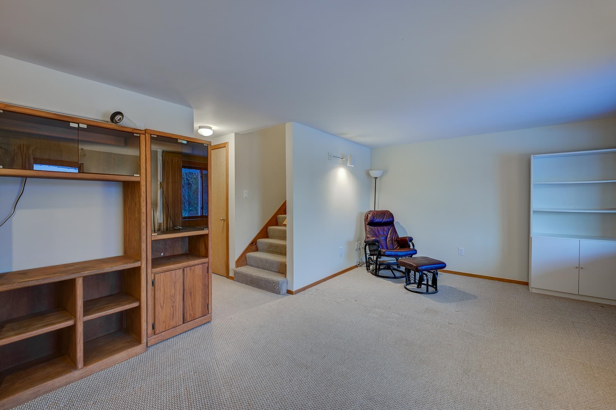 Carpeted living area with built-in wooden shelving, a leather recliner, and stairs.