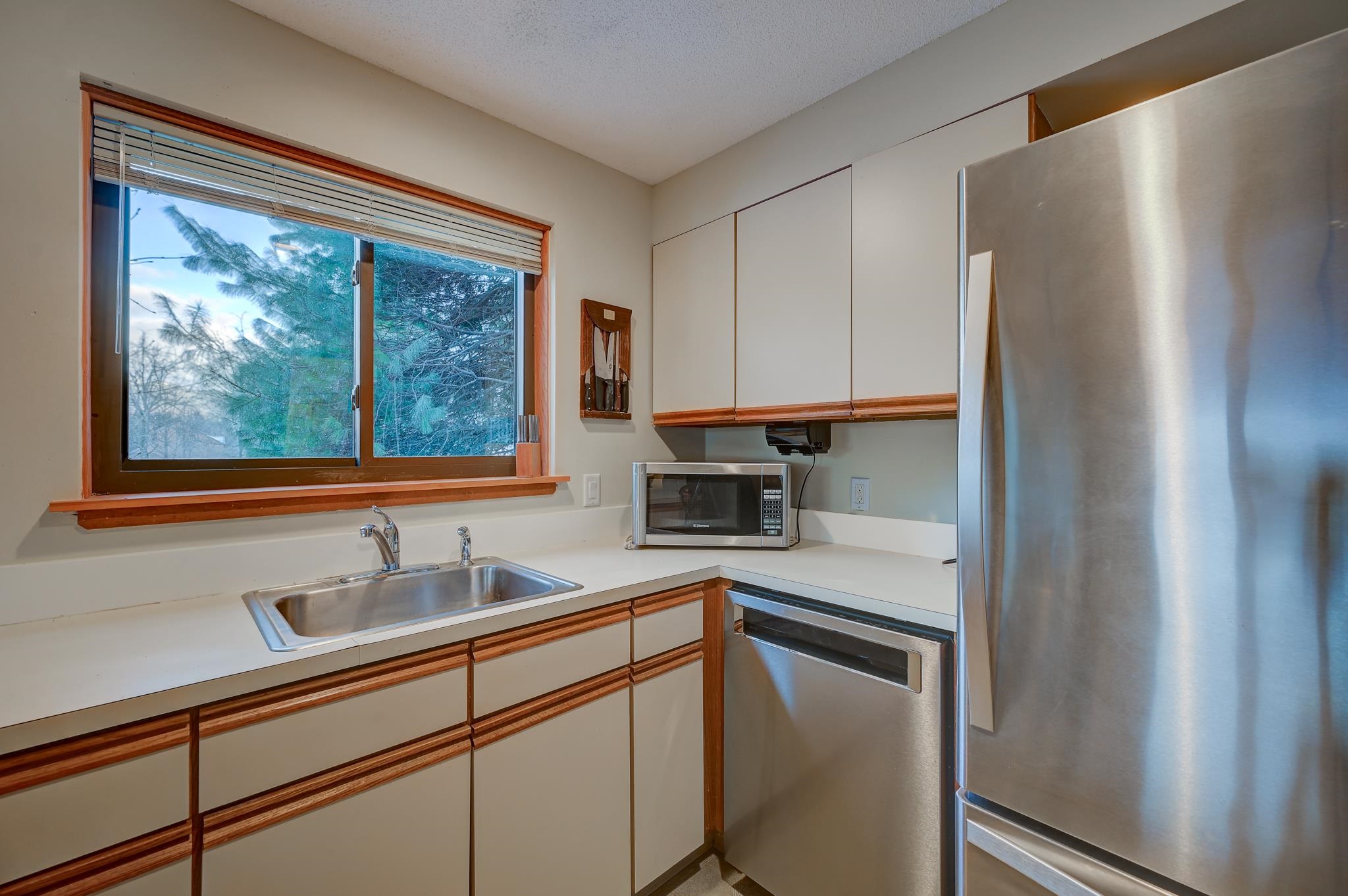 Kitchen with cream cabinets and wood trim, stainless-steel appliances, and a window overlooking trees.