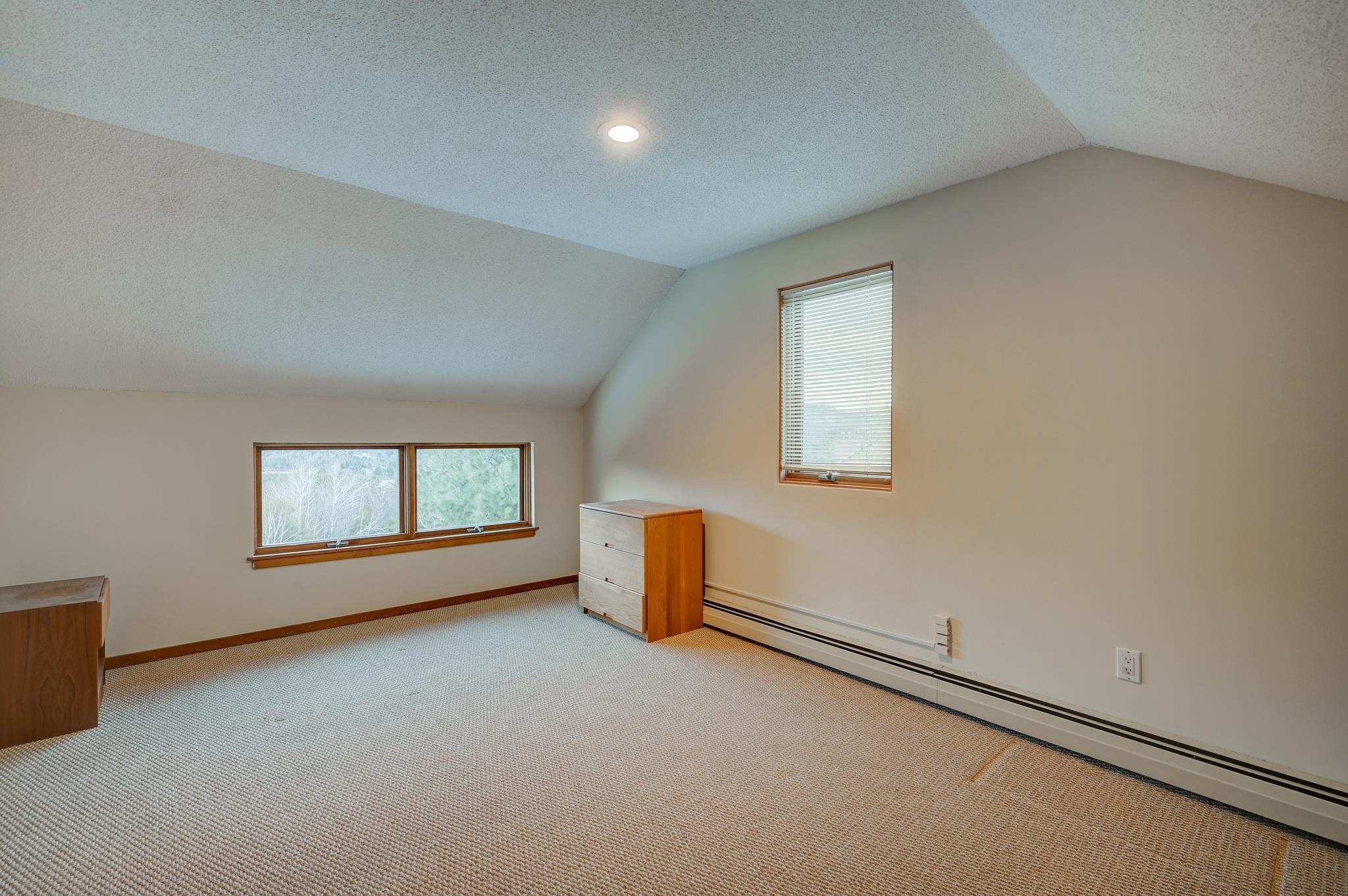 Carpeted room with a sloped ceiling, three windows, and a small wooden chest of drawers.