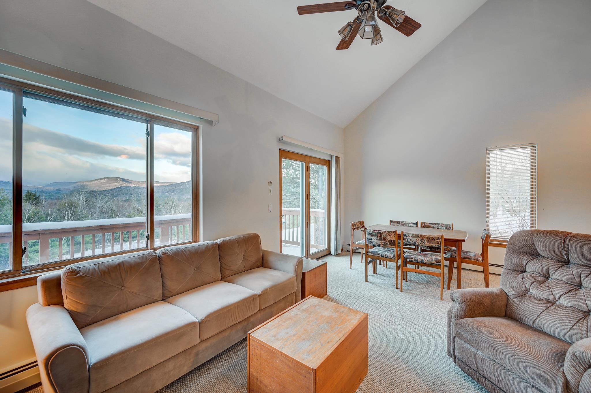 Furnished living and dining area with large windows overlooking forested mountains.
