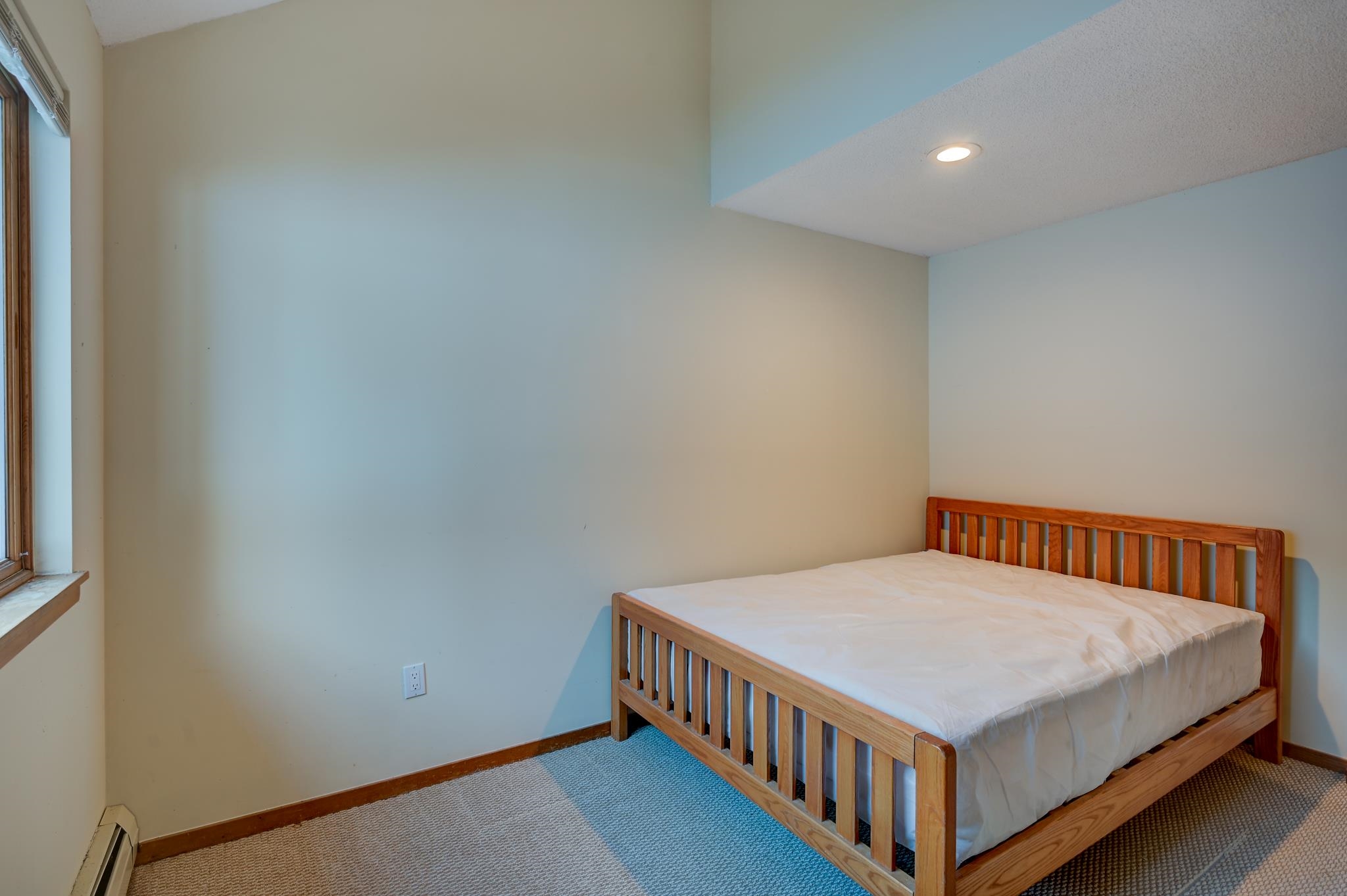 Bedroom with a wooden slatted bed, white bedding, and a wood-trimmed window.