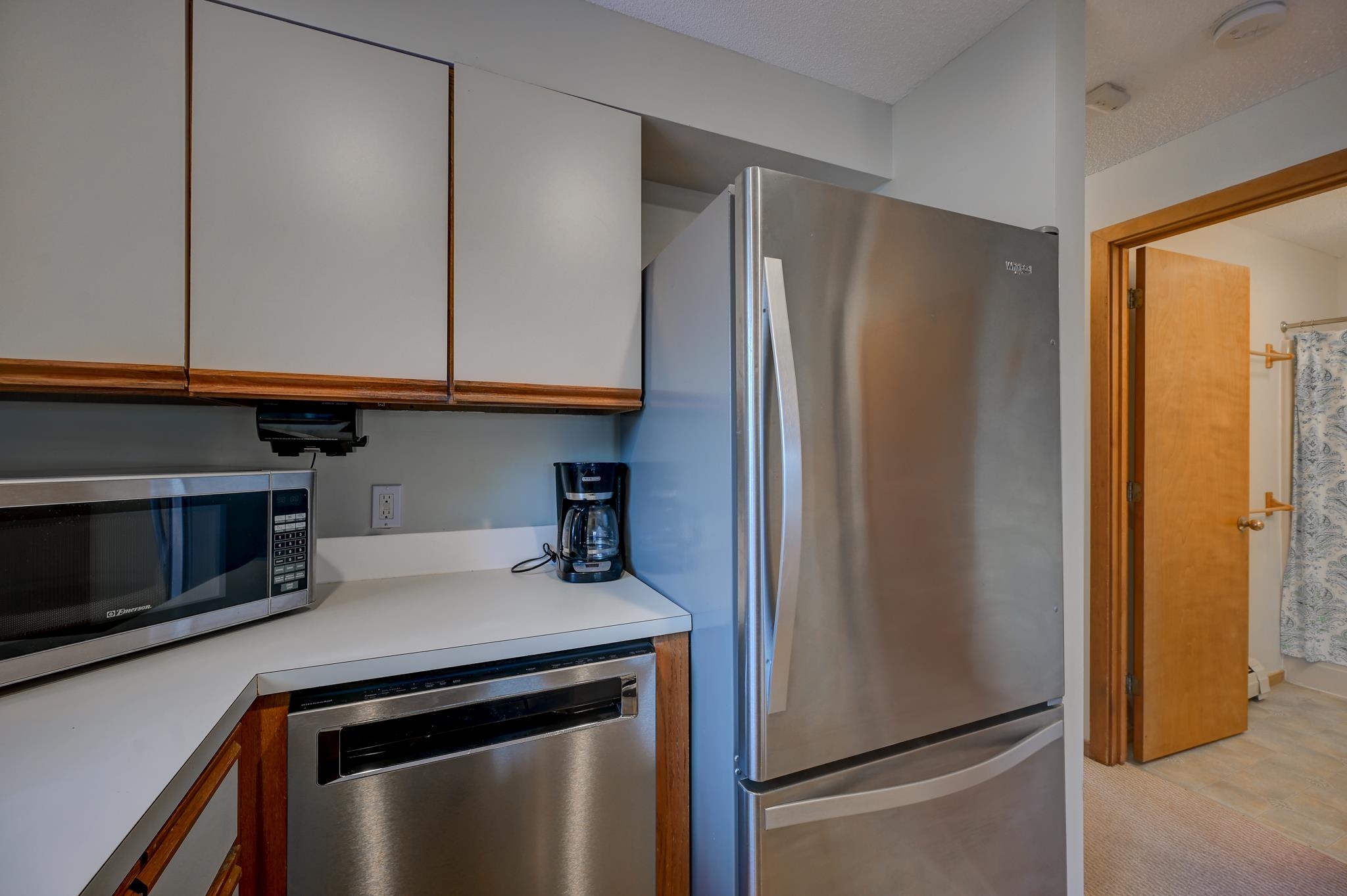 Kitchen with stainless steel appliances and white countertops, viewed beside an open bathroom doorway.